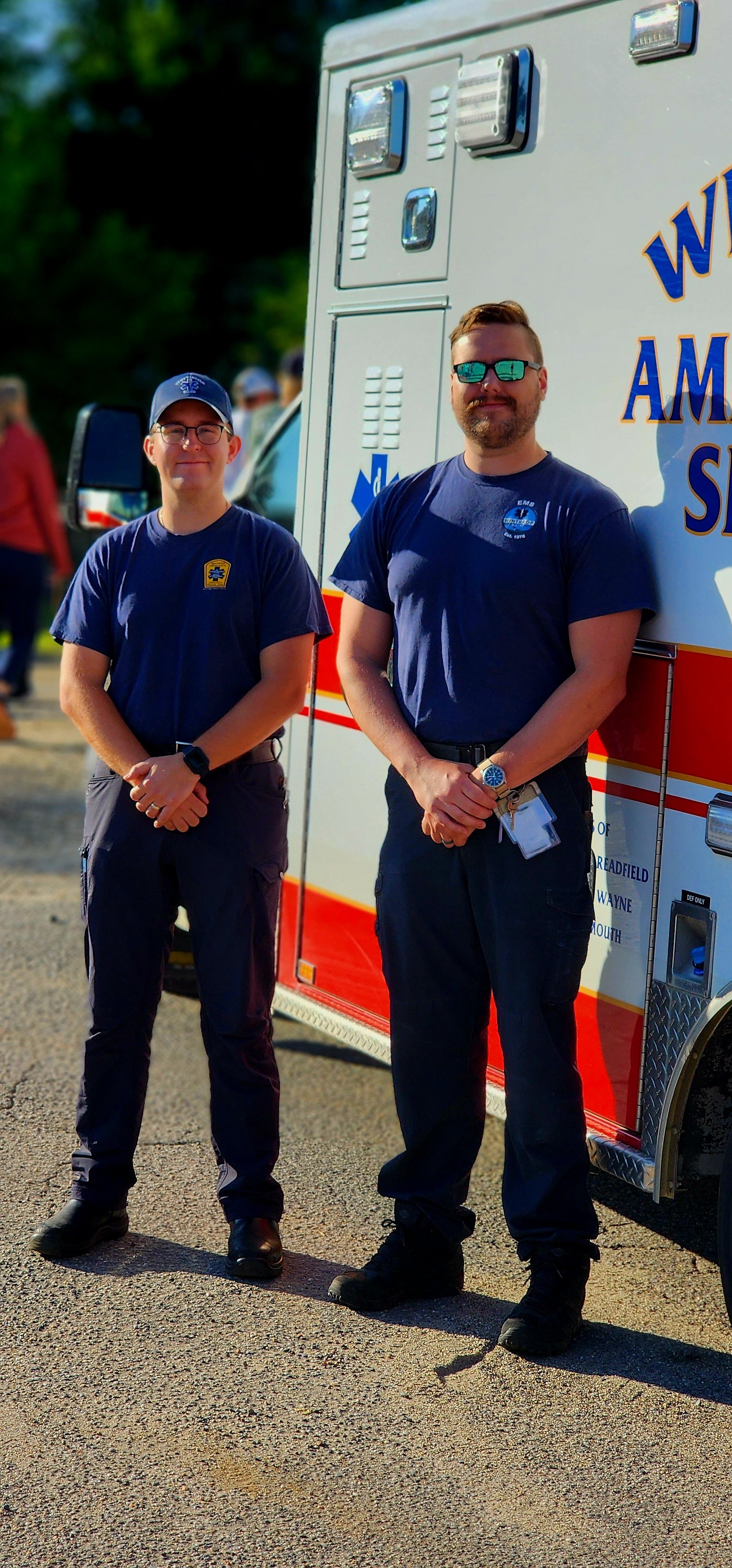 Two men in EMT uniforms standing in front of an ambulance