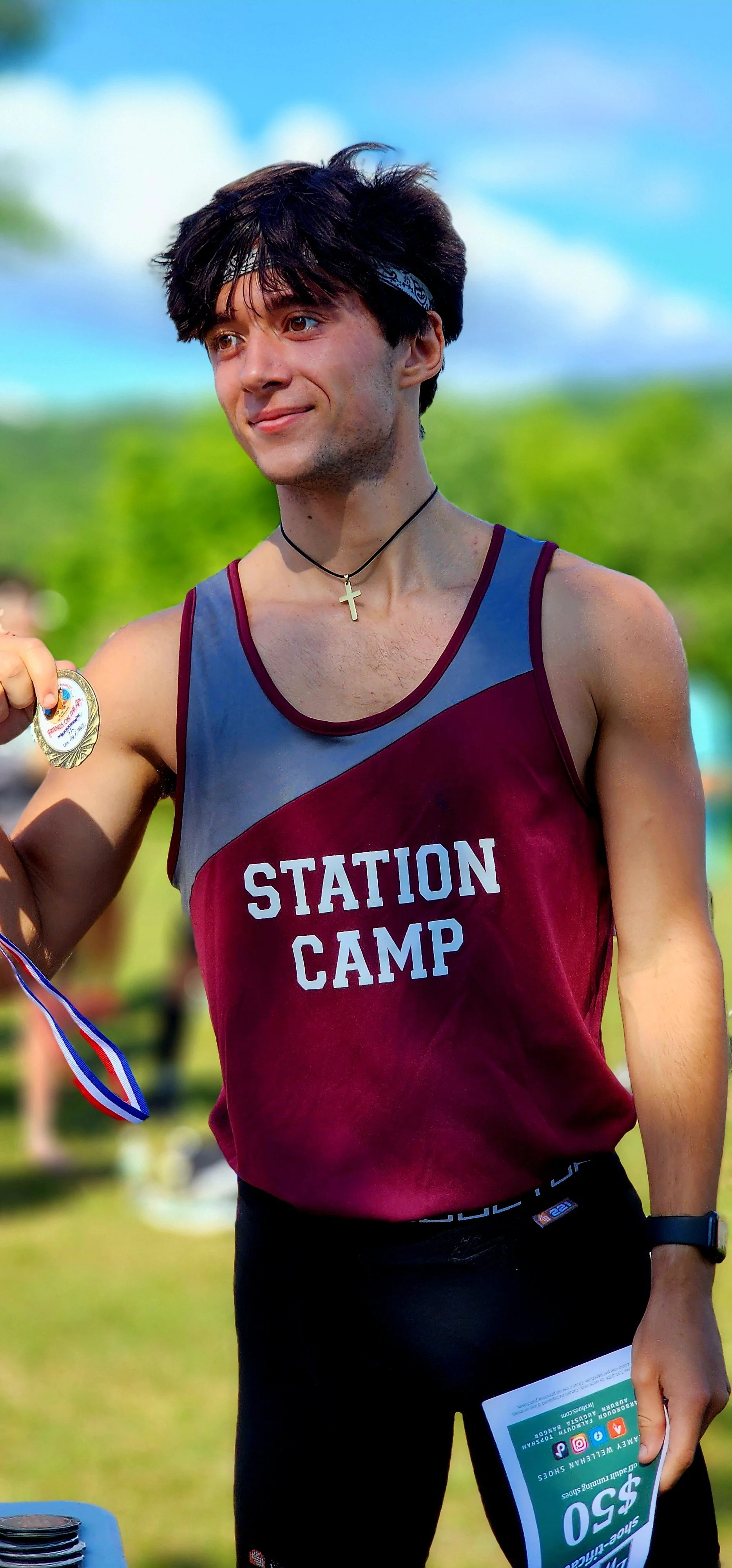A man wearing a maroon and grey tank top and black shorts behind handed a prize medal