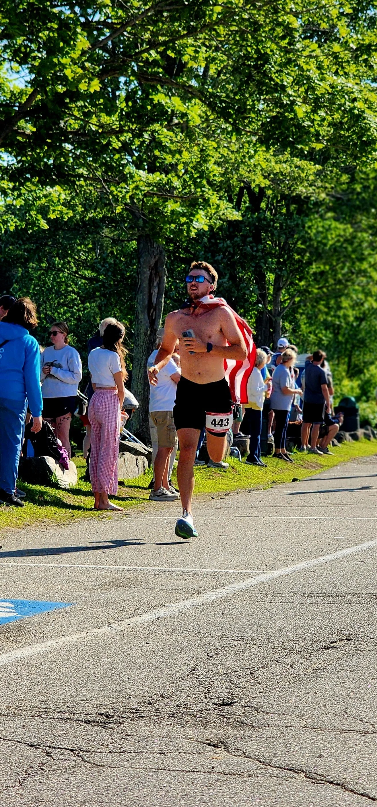 A shirtless man wearing black shorts running with a crowd standing in the backgrounf