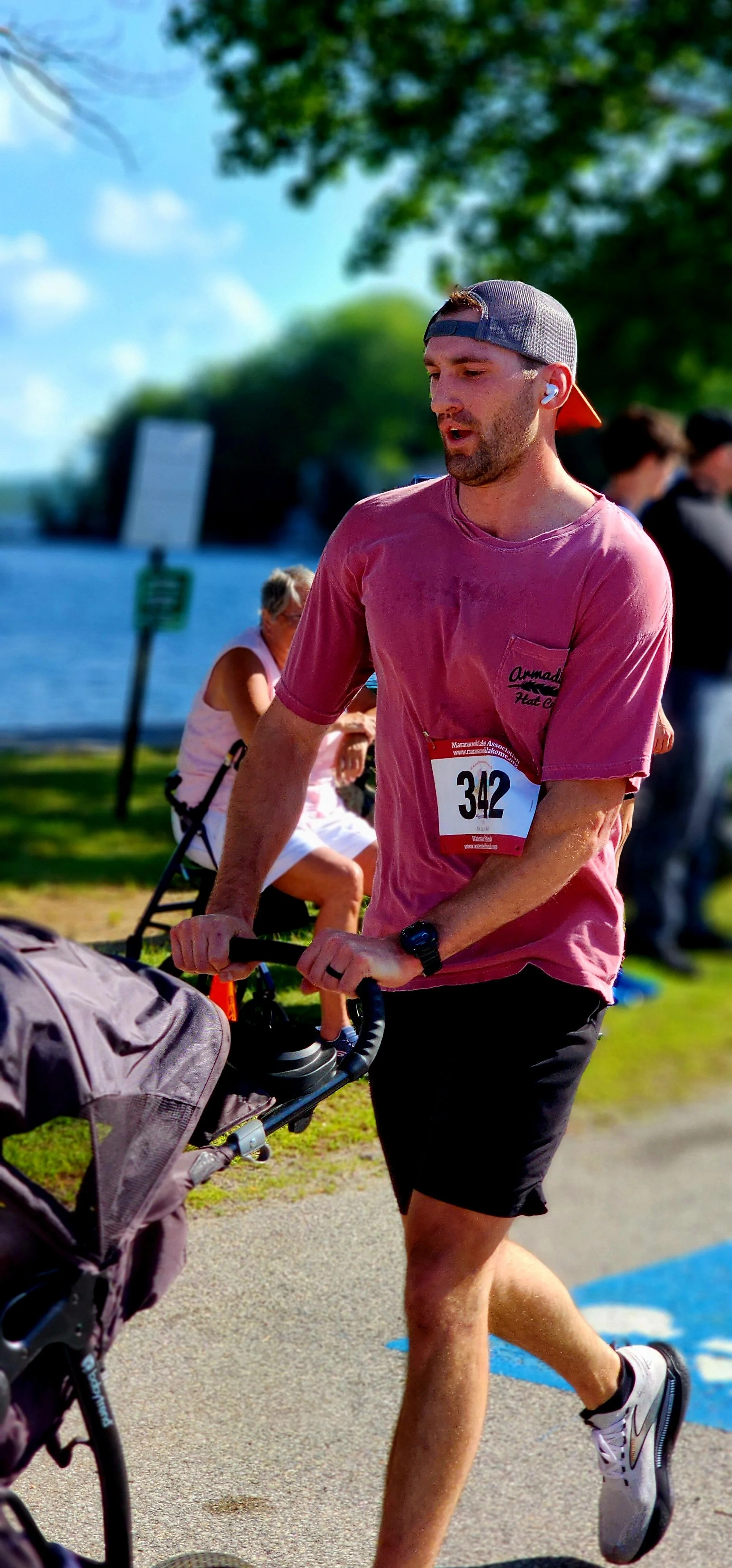 A man wearing a red t-shirt and black shorts running and pushing a stroller