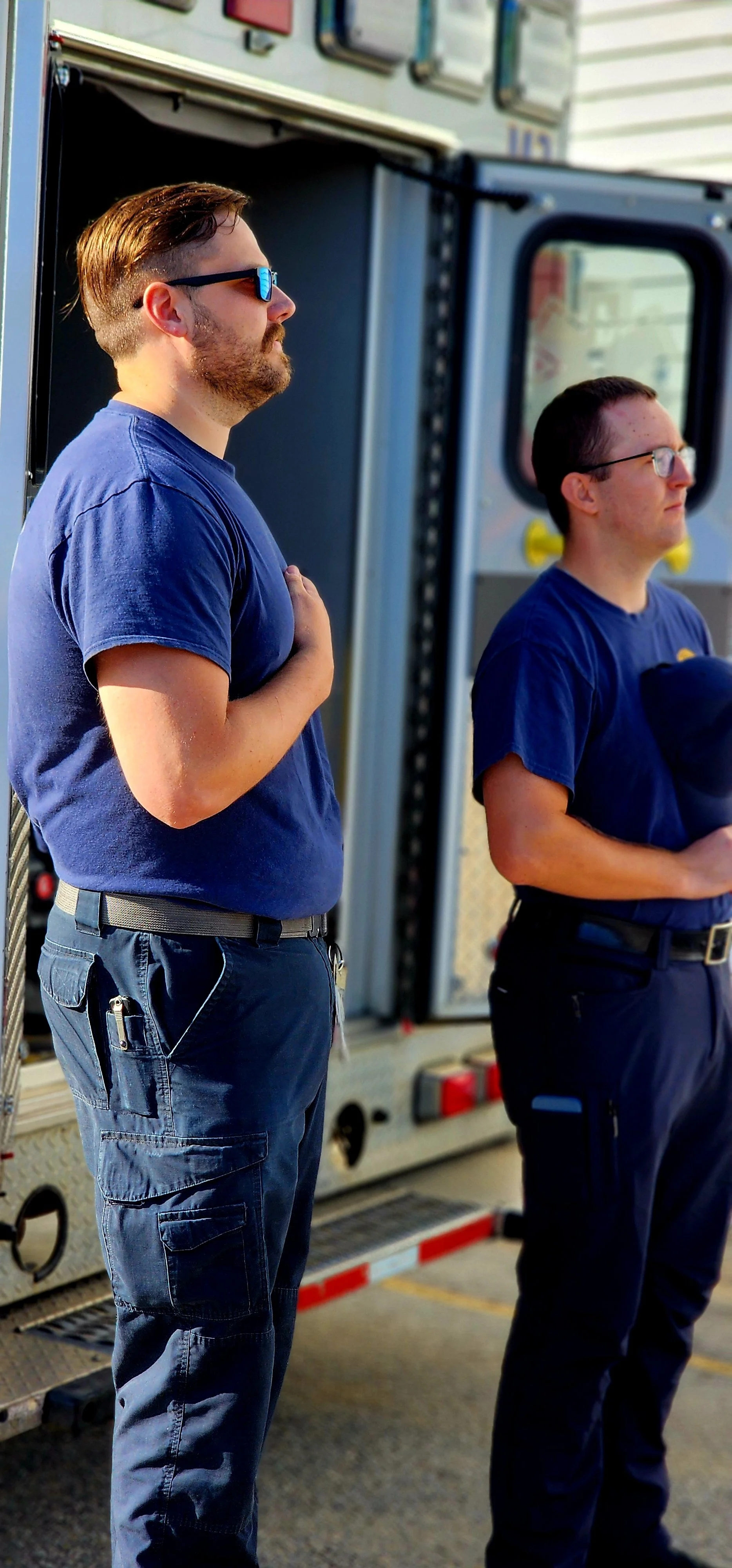 Two men in EMT uniforms with their hands resting over their hearts