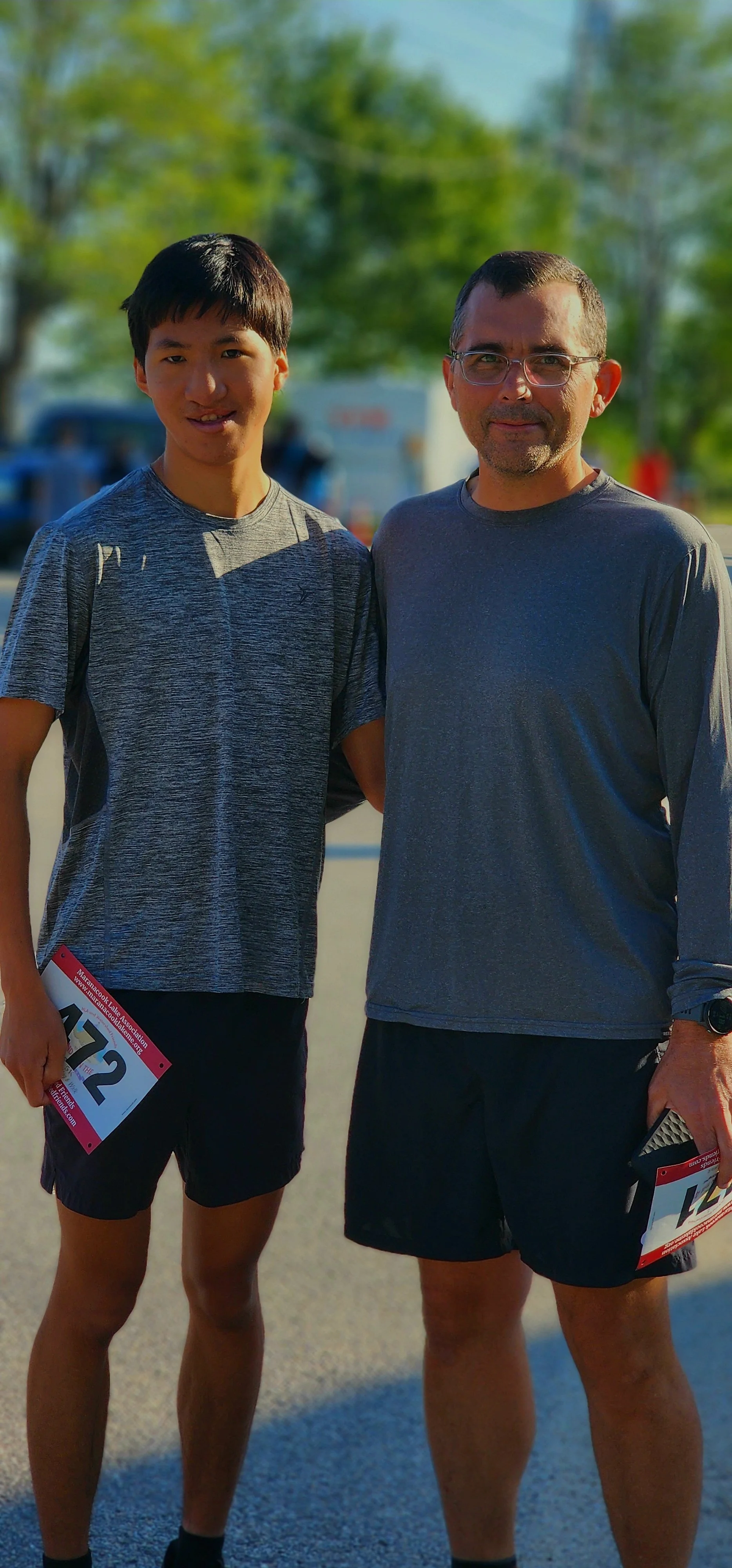 Two men, wearing grey shirts and black shorts, smiling at the camera