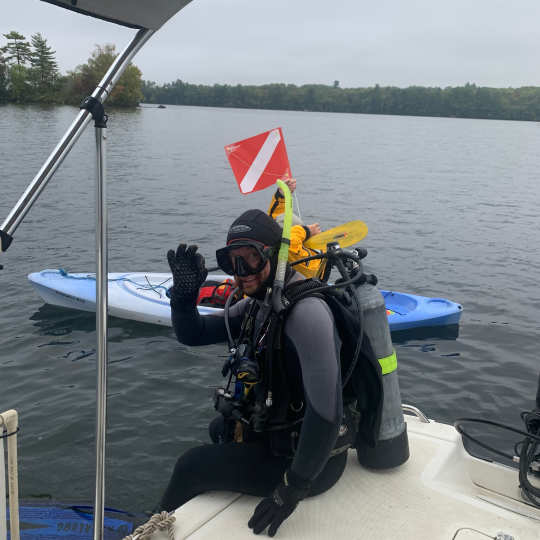 A SCUBA diver sitting on the edge of a boat waving at the camera
