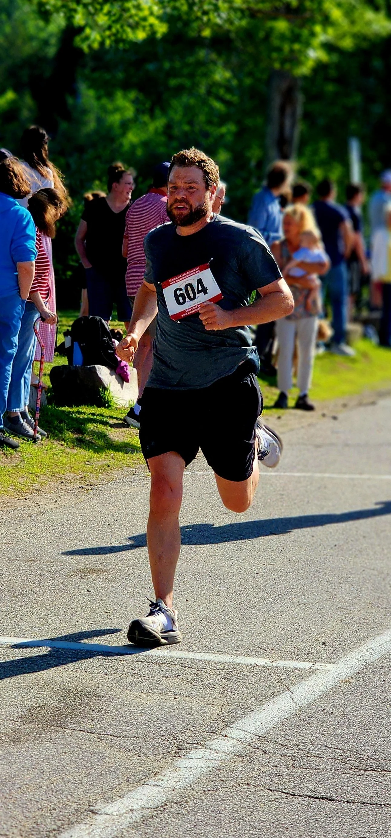A man wearing a dark blue t-shirt and black shorts running with a crowd standing in the background
