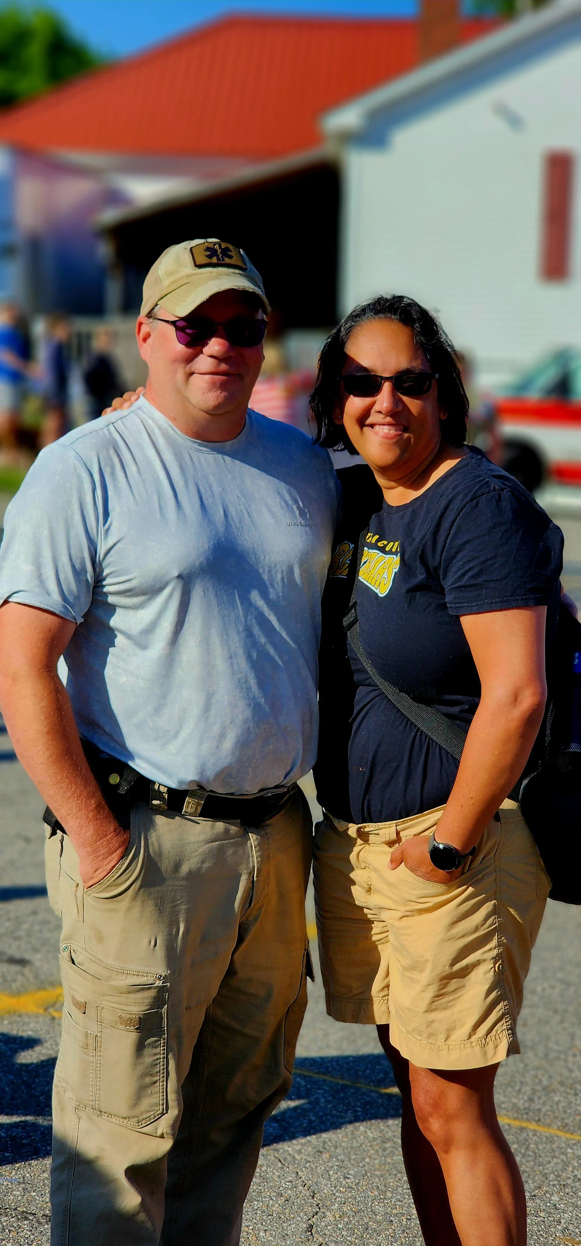 A man, in a grey t-shirt and khaki pants, and a woman, wearing a navy t-shirt and khaki shorts, smiling at the camera