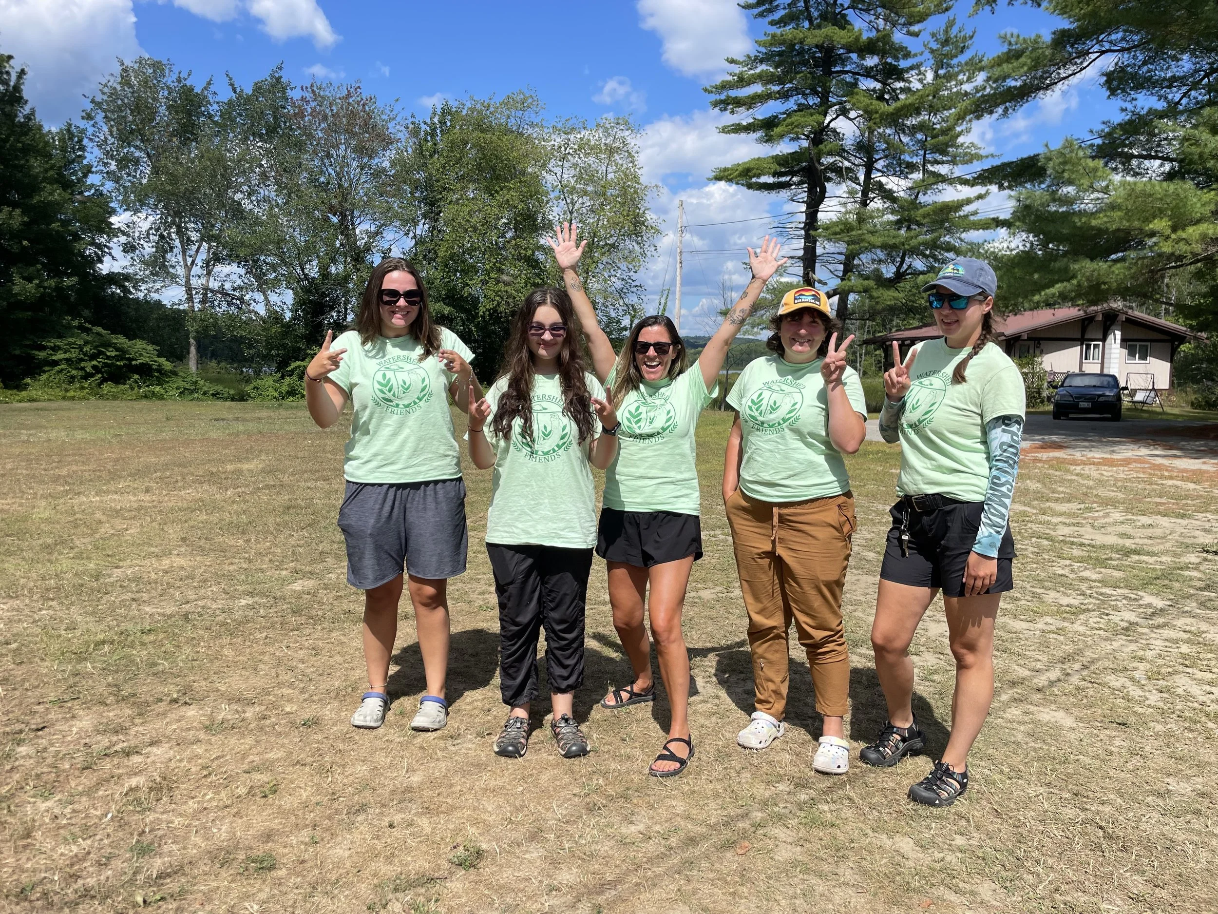 Five people lined up smiling at the camera in matching green shirts