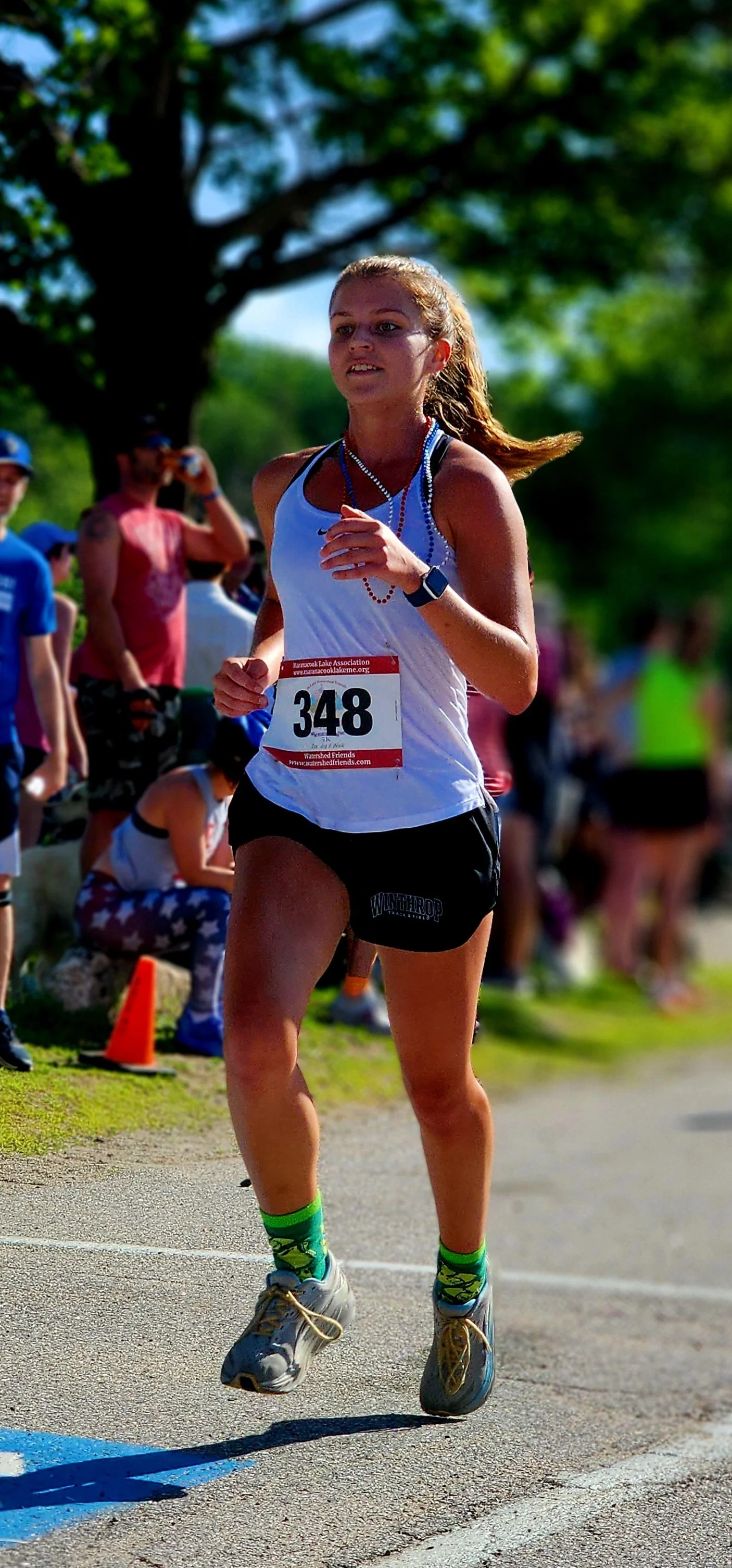 A woman wearing a white tank top and black shorts running with a crowd standing in the background