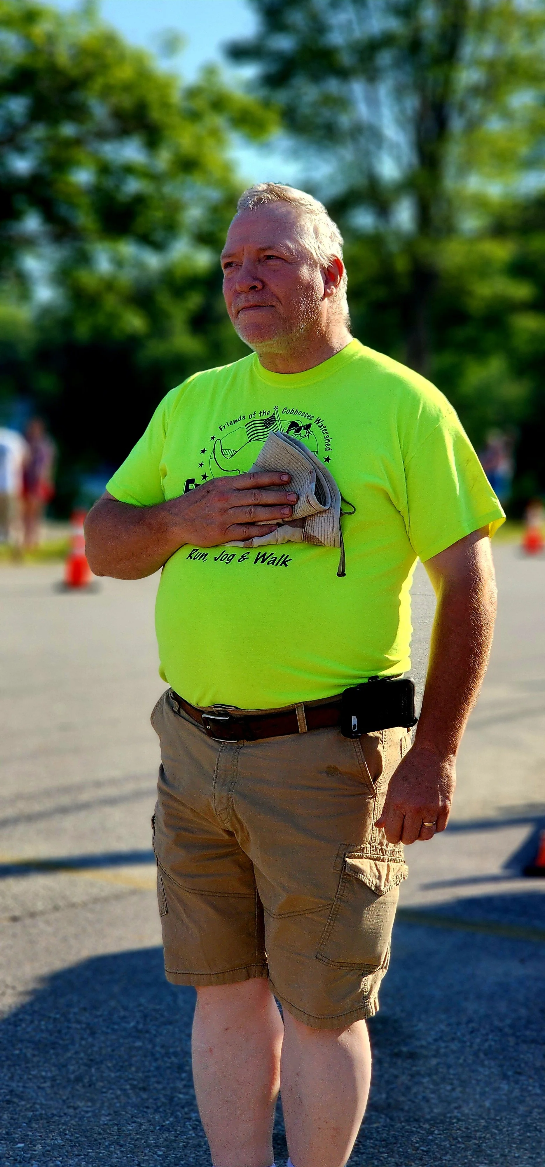 A man, wearing a neon yellow shirt and khaki shorts, with his right hand resting on his chest