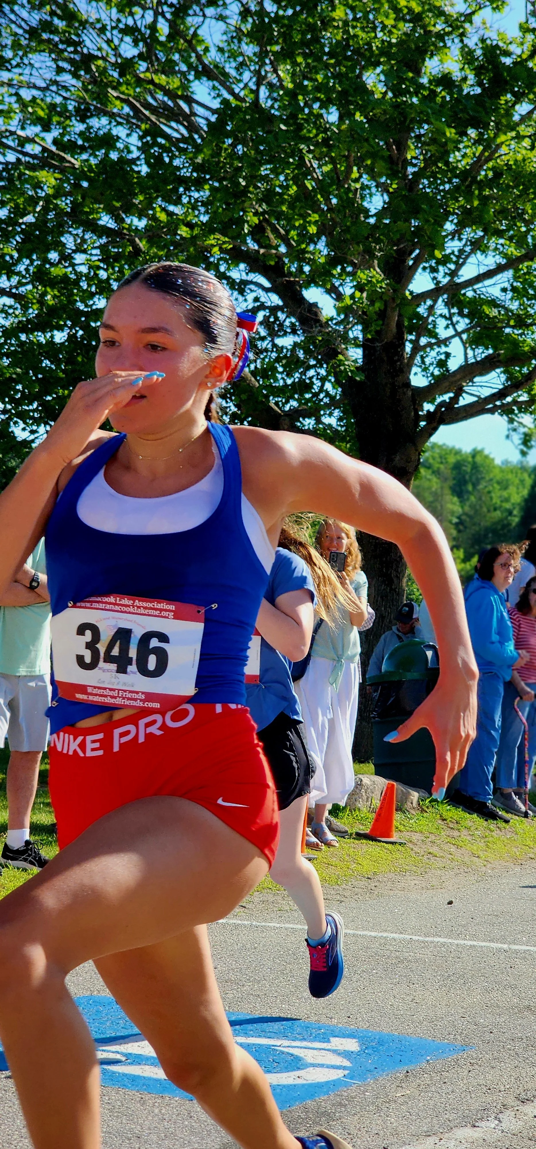 A woman wearing a blue tank top and red shorts running with a crowd standing in the background