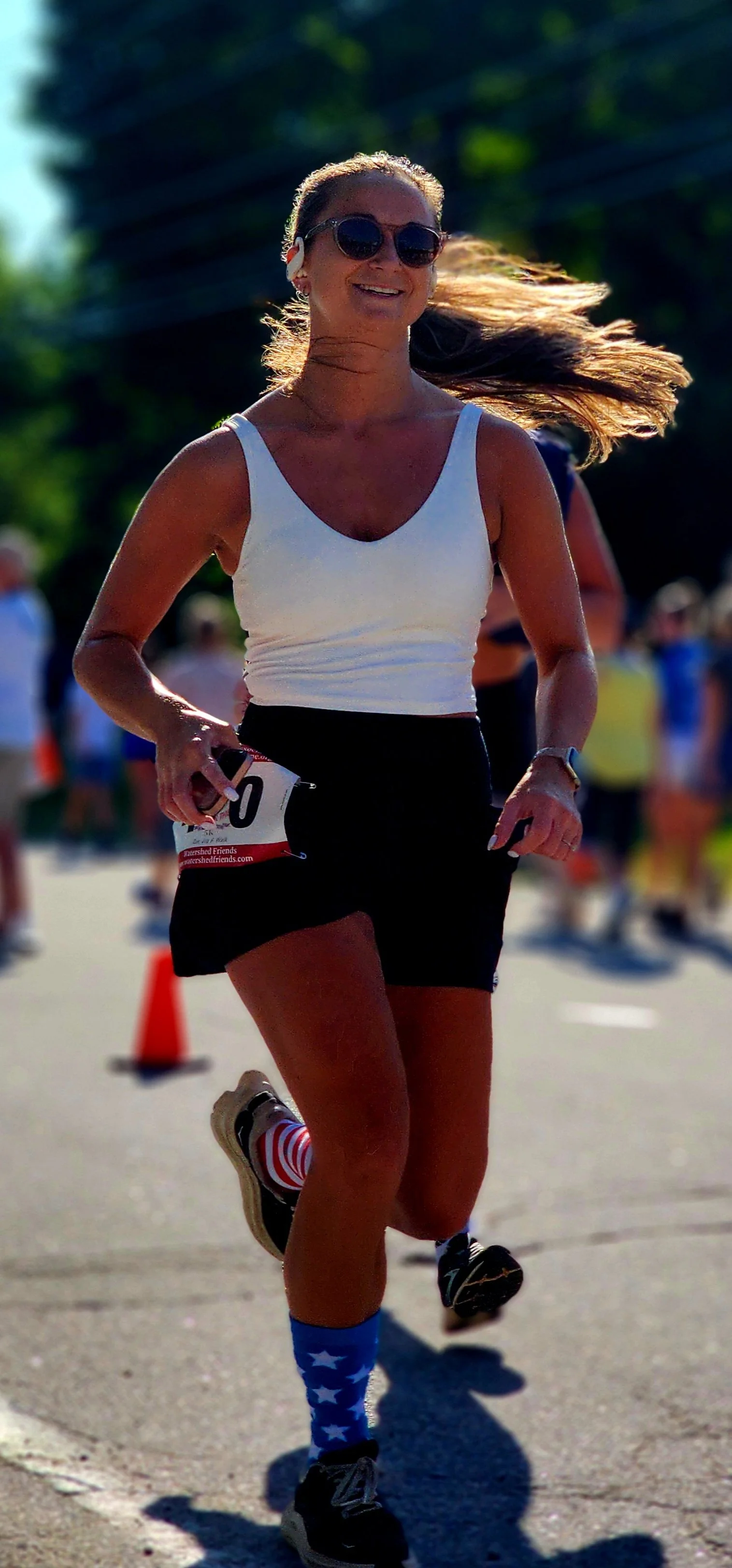 A woman wearing a white tank top and black shorts running