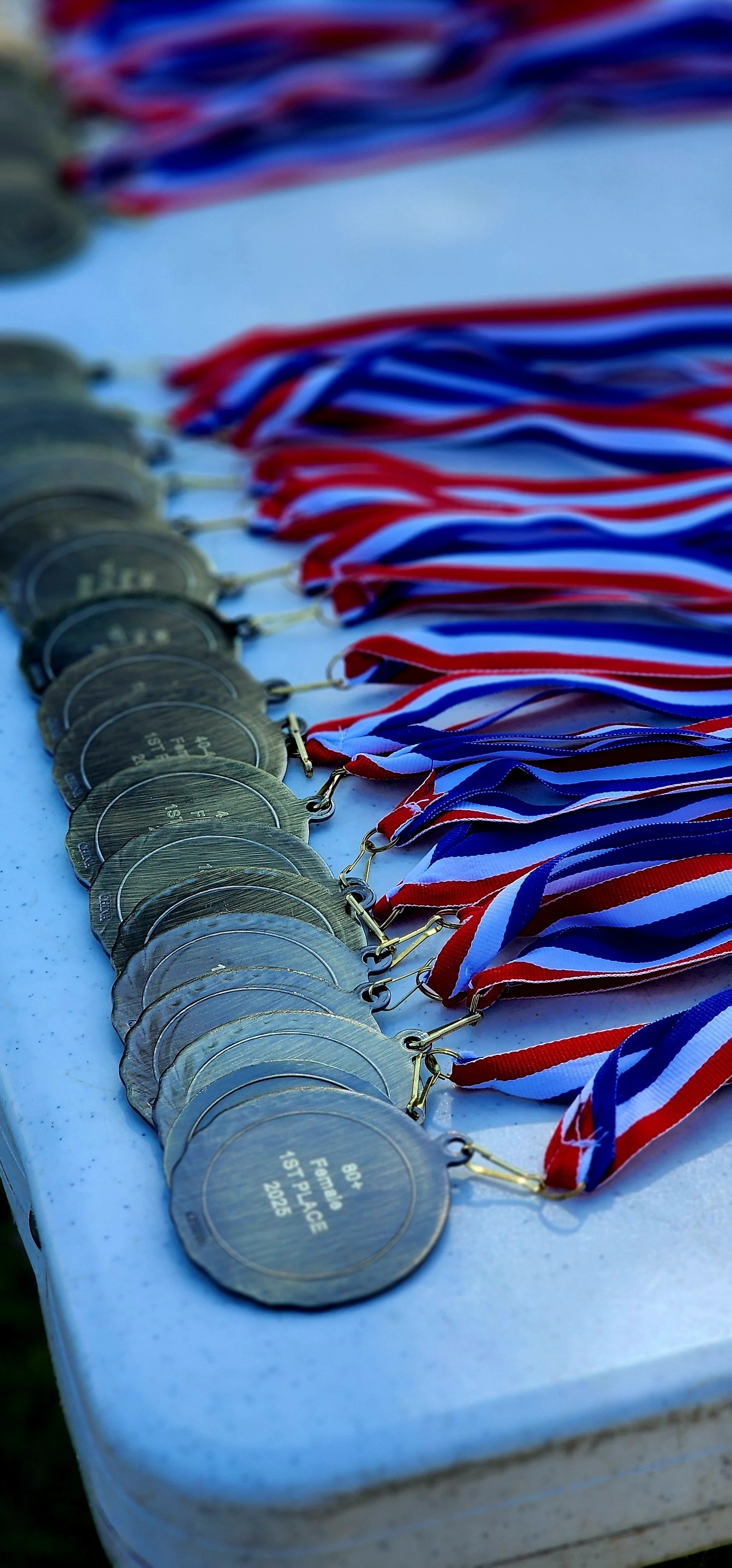 A close-up view of award medals, the one on the top of the pile says "80+ female first place, 2025"
