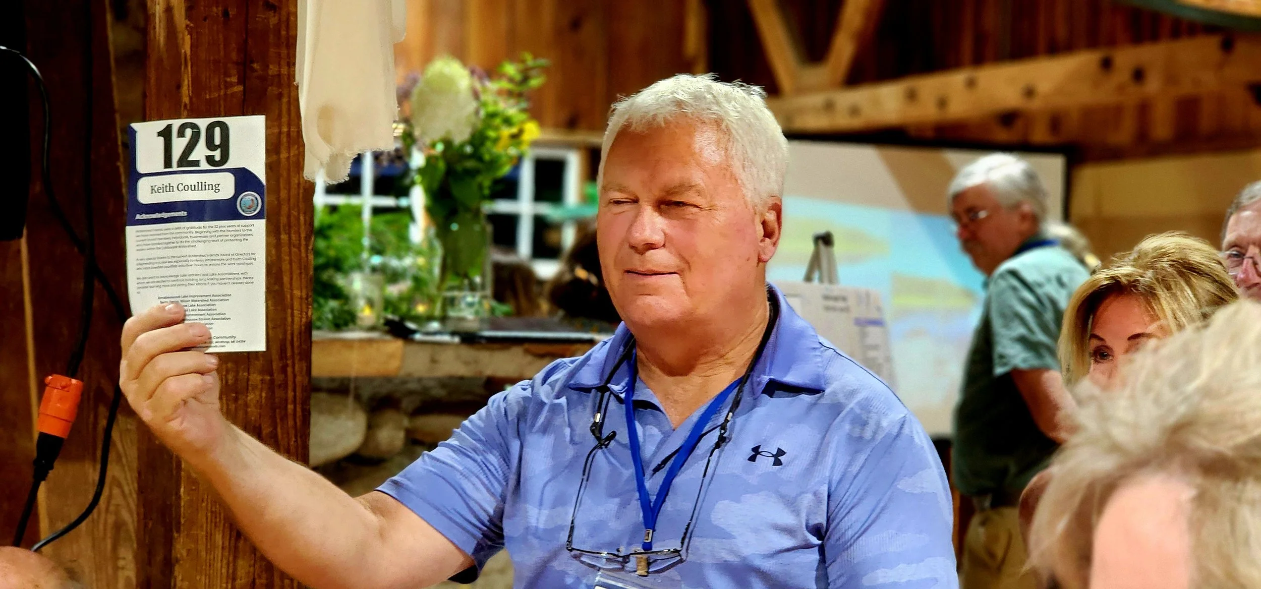 A man, wearing a light blue polo, looking off camera, holding up the event program