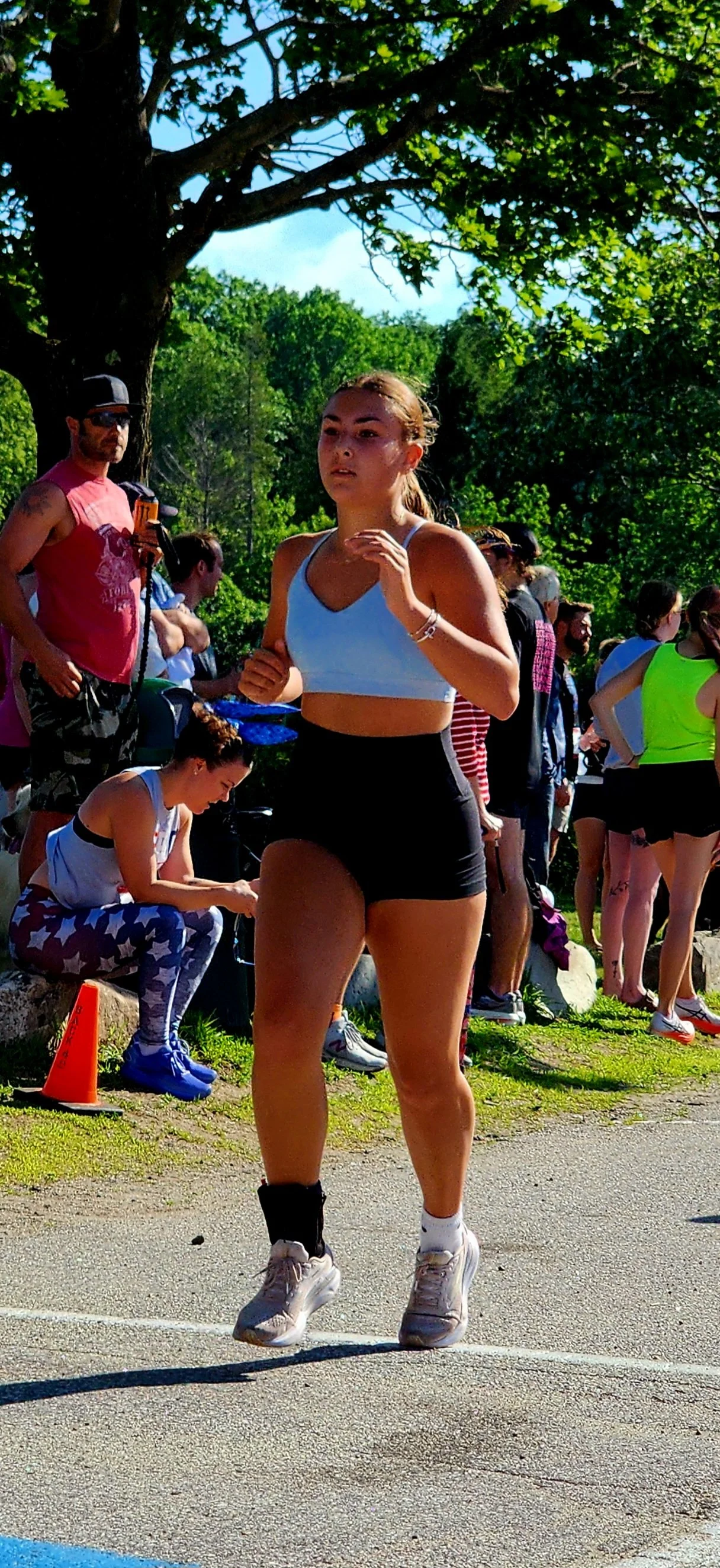 A woman wearing a white sports bra and black shorts running with a crowd standing in the background