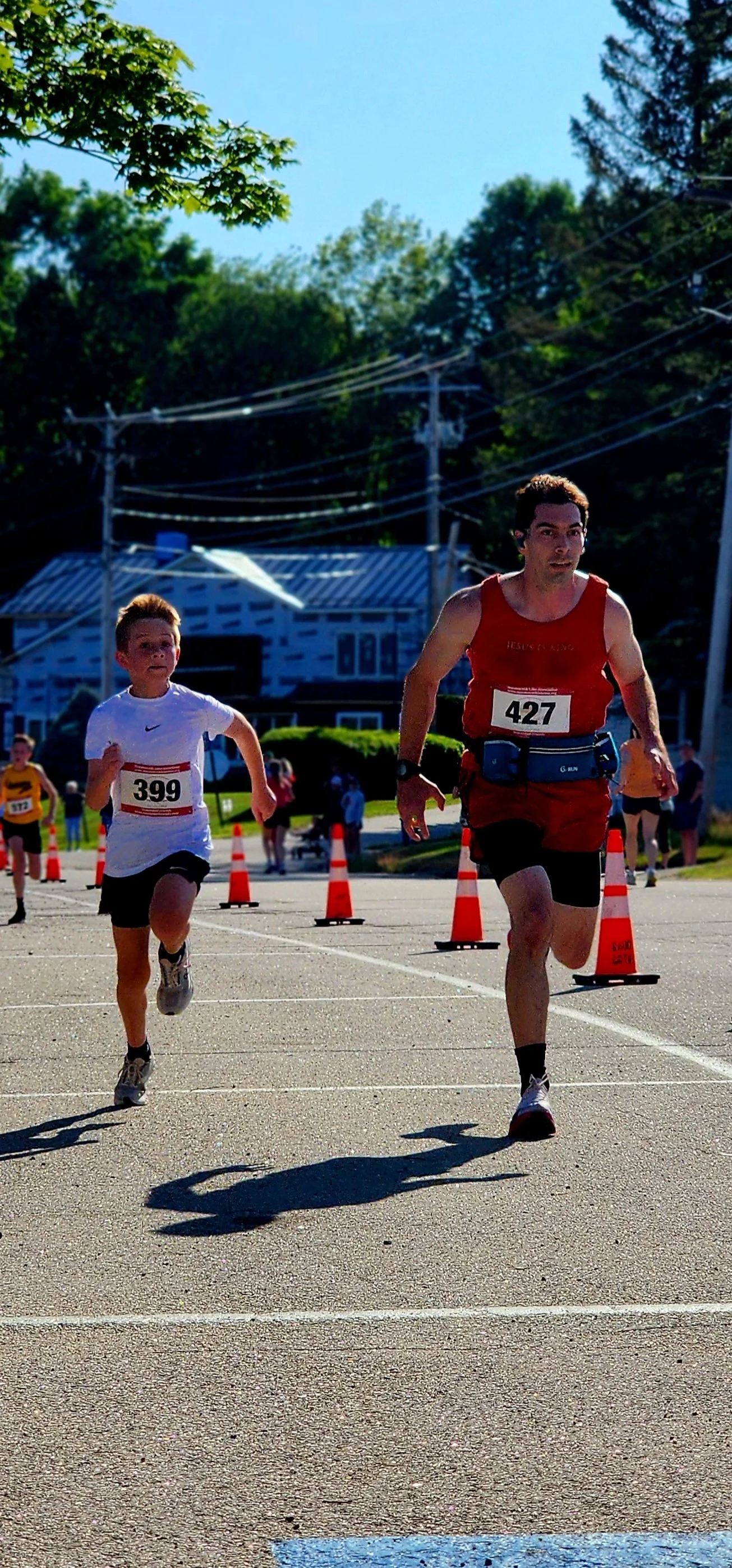 A boy wearing a white t-shirt and black shorts running next to a man wearing a red tank top and shorts