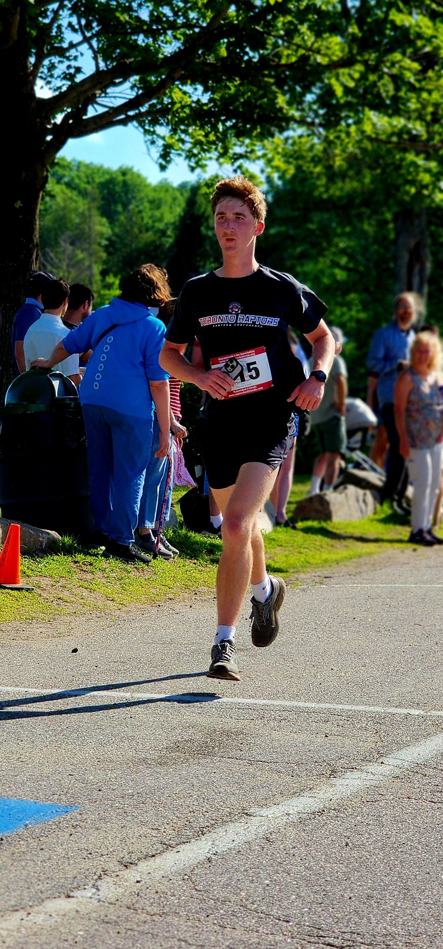A man wearing a black t-shirt and shorts running with a crowd standing in the background