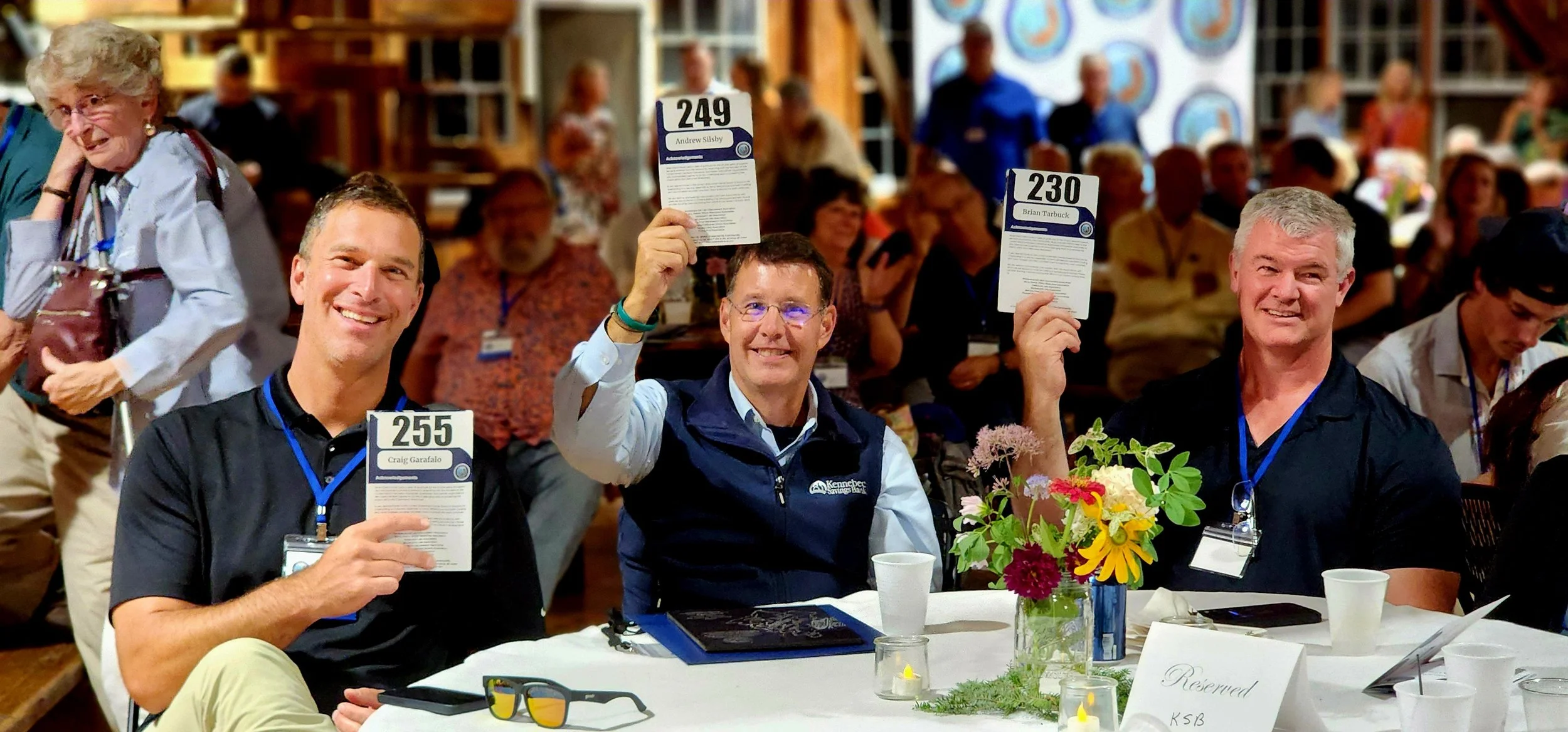 Three men sitting at a table holding up event programs