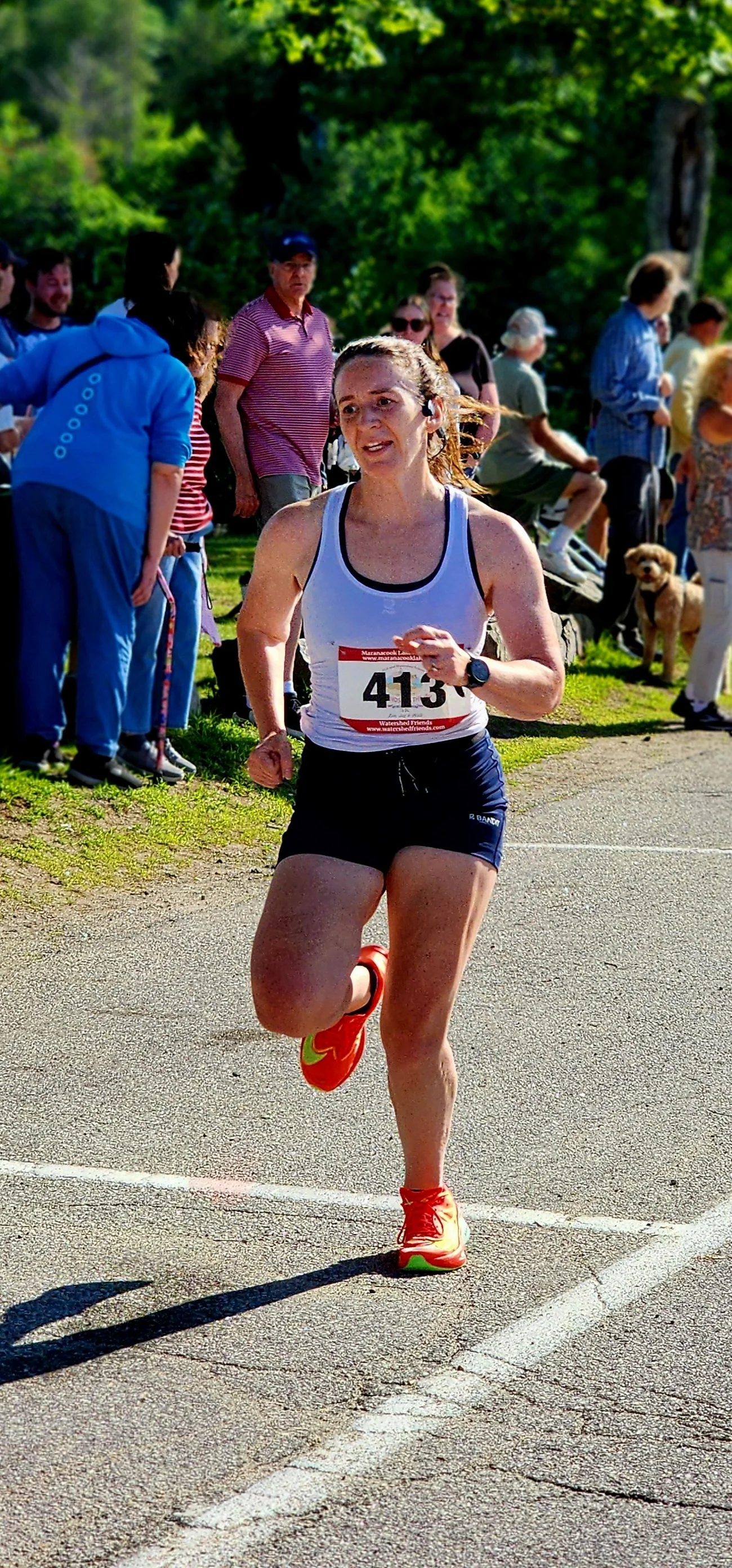 A woman wearing a white tank top and black shorts running with a crowd standing in the background