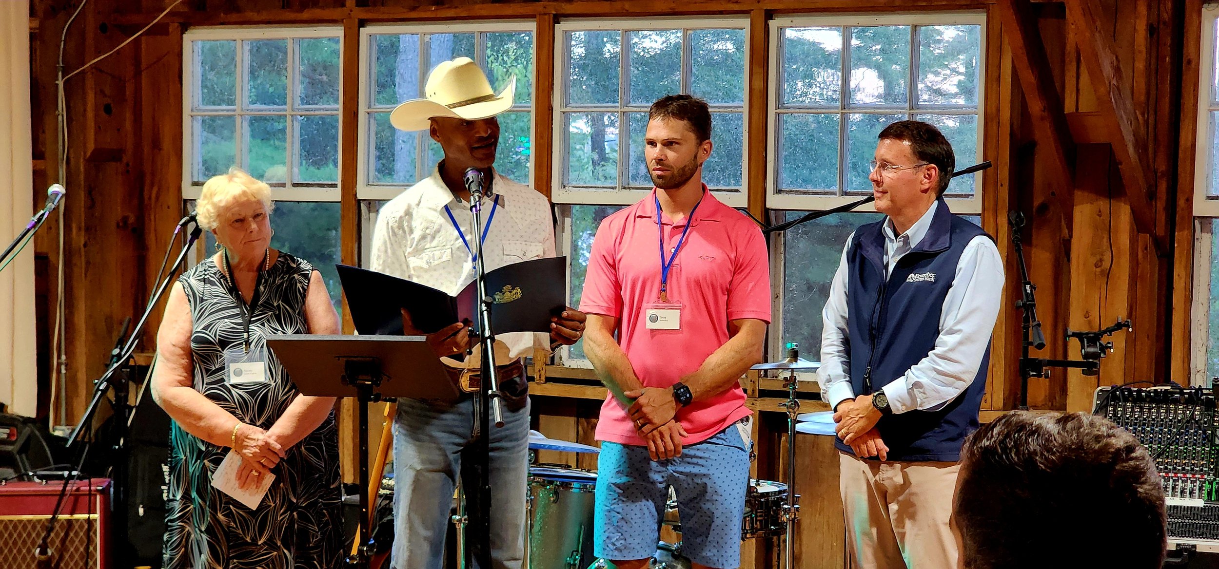 A woman and three men, the left-most man is speaking into a microphone