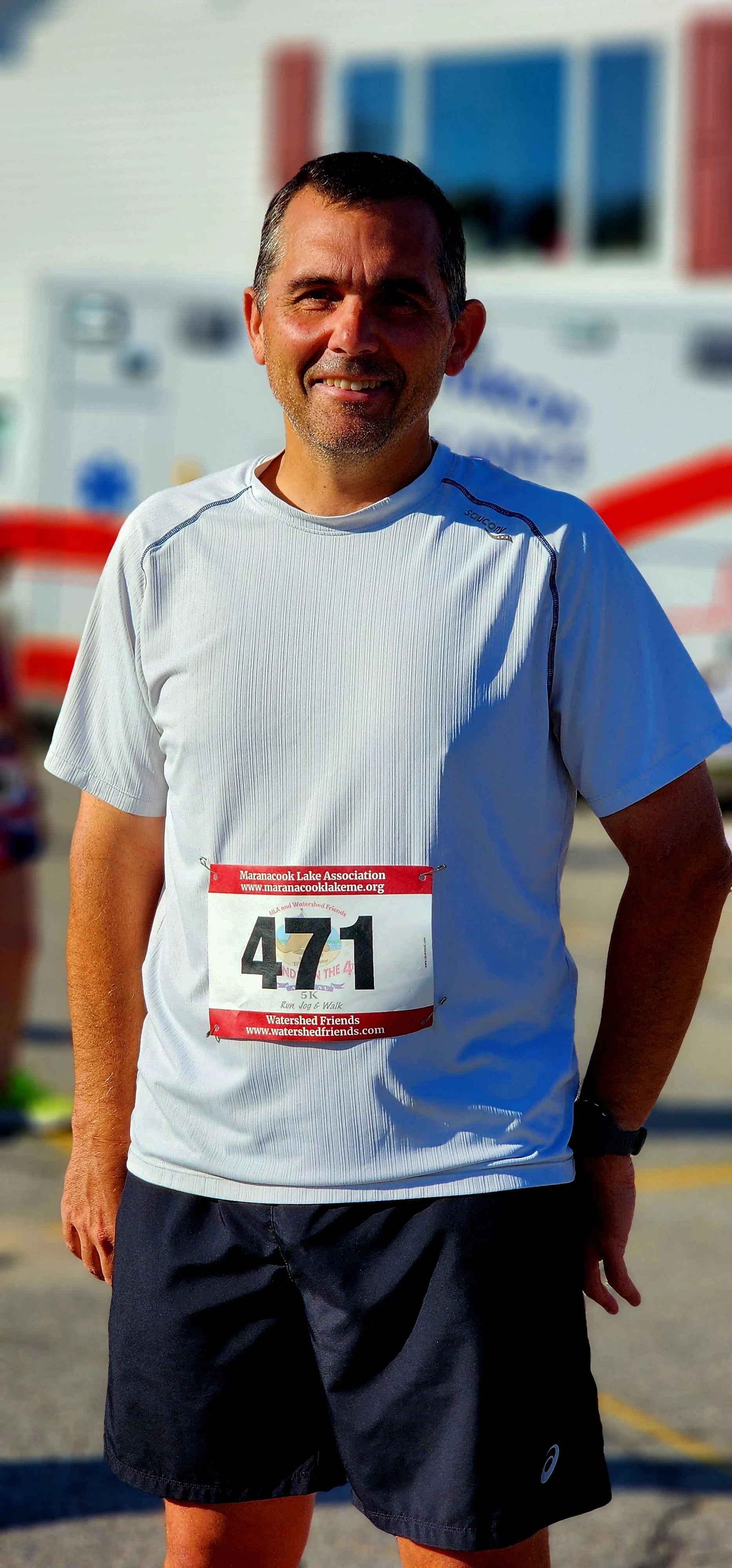 A man, wearing a white shirt and black shorts, smiling at the camera