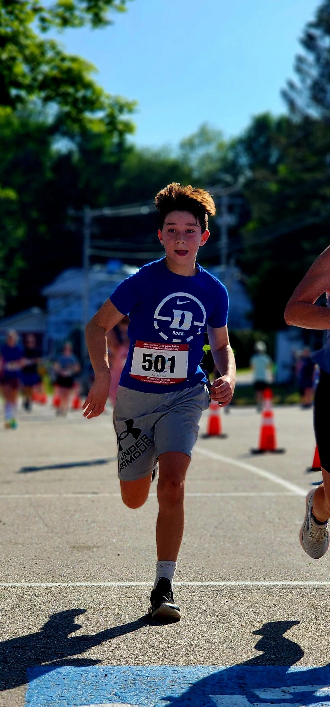 A boy wearing a blue t-shirt and grey shorts running