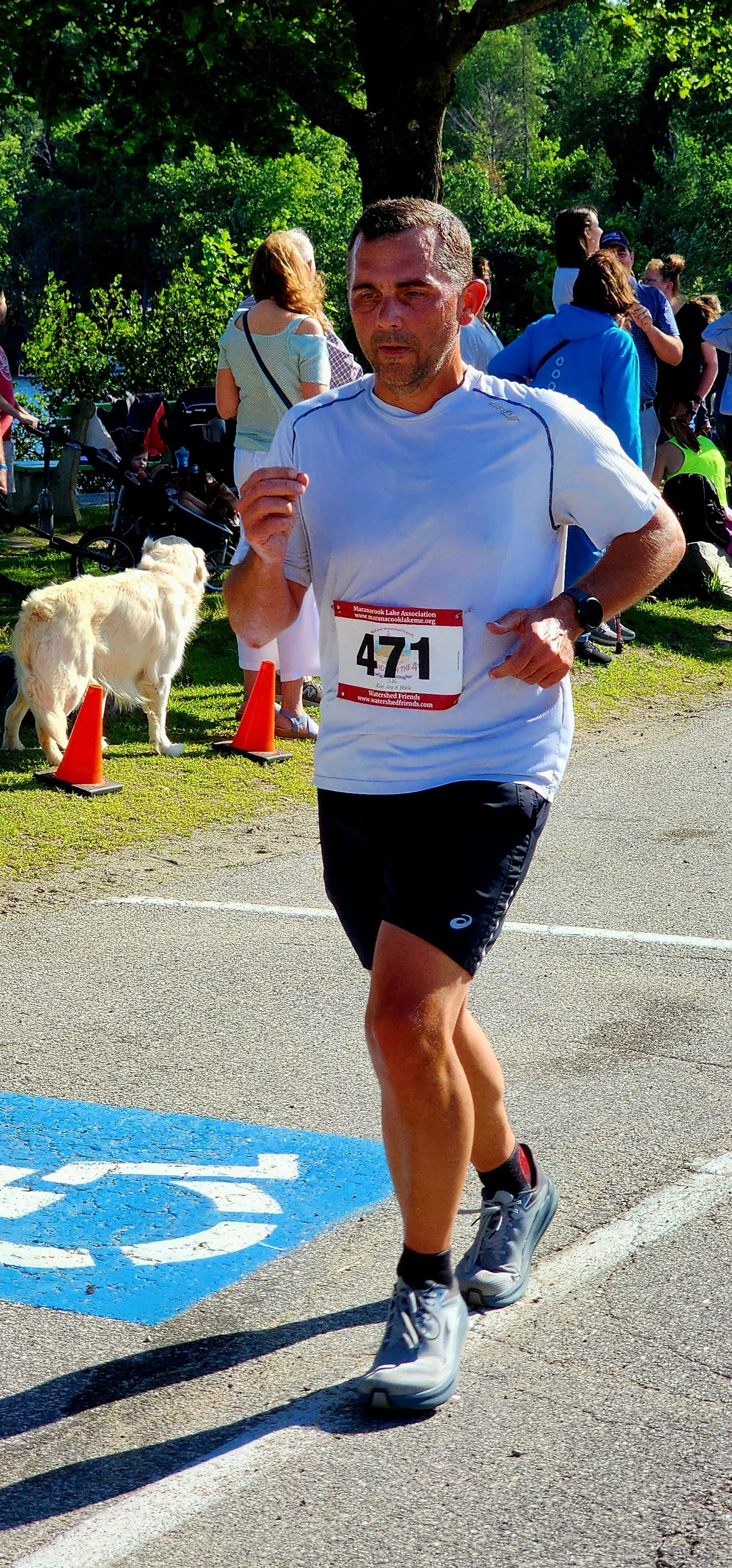 A man wearing a white t-shirt and black shorts running with a crowd standing in the backgrounf 