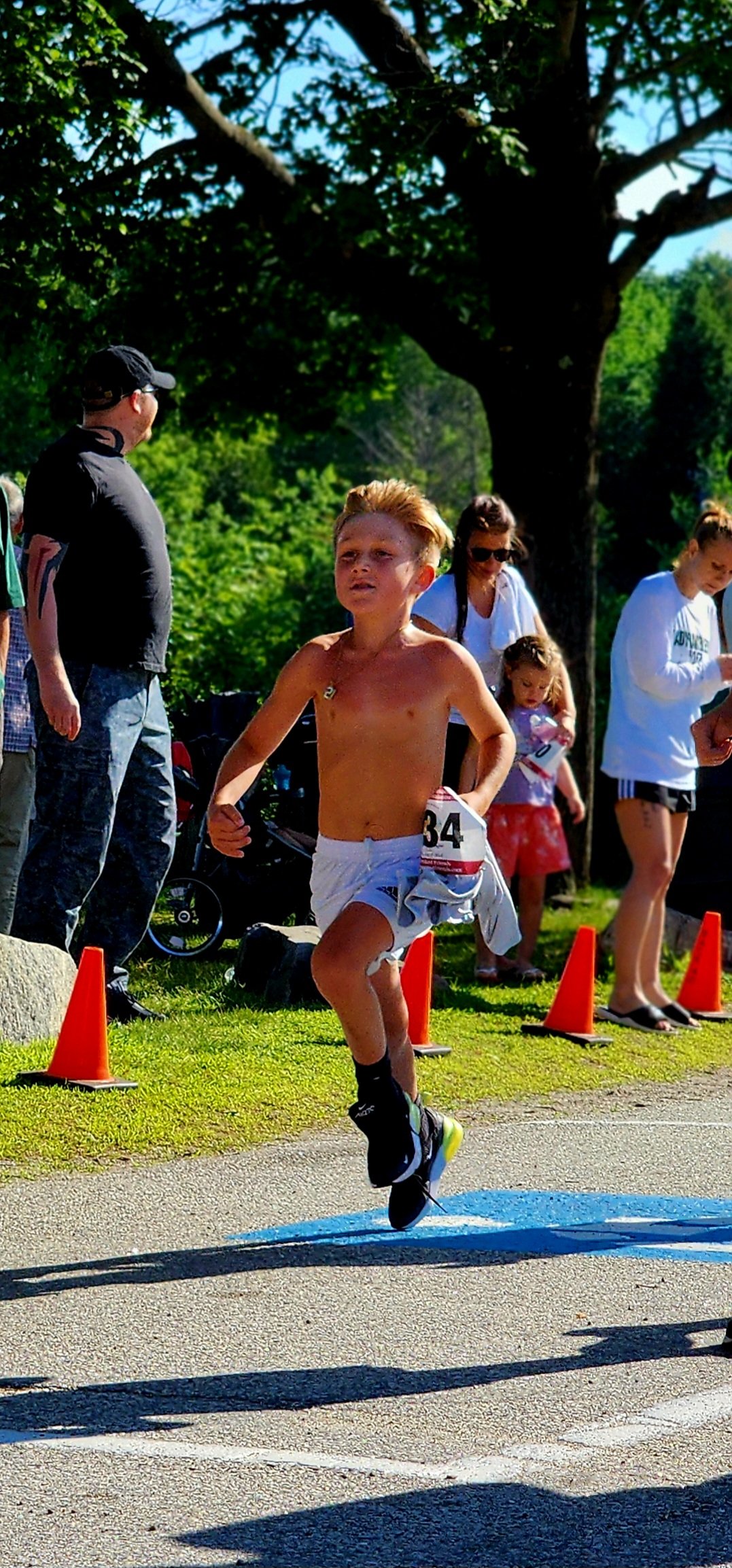 A shirtless boy wearing white shorts running with a crowd standing in the background