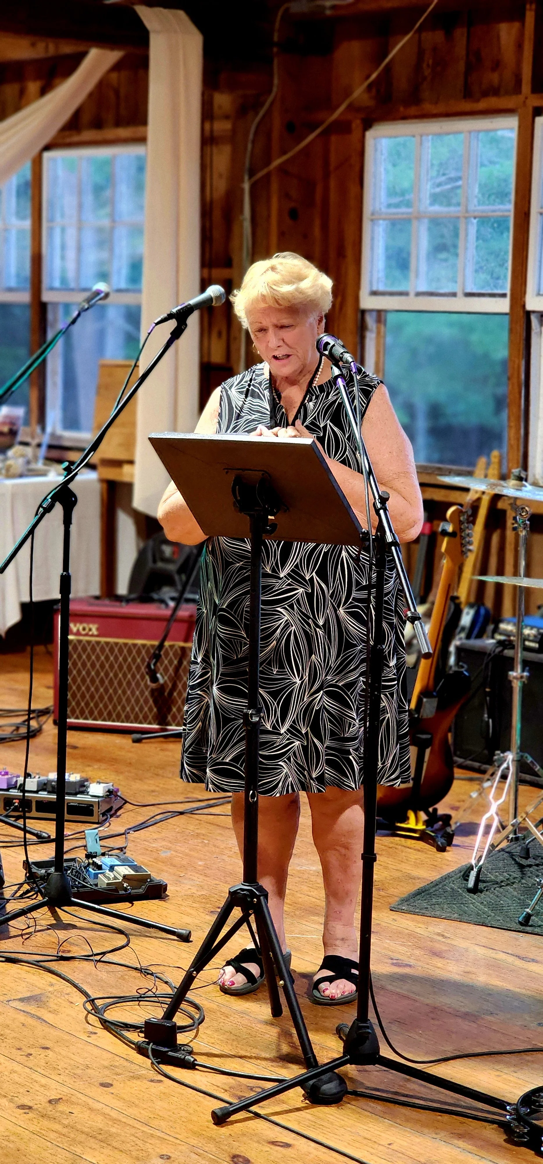 A woman, wearing a black dress with white patterns, speaking into a microphone with a stand in front of her