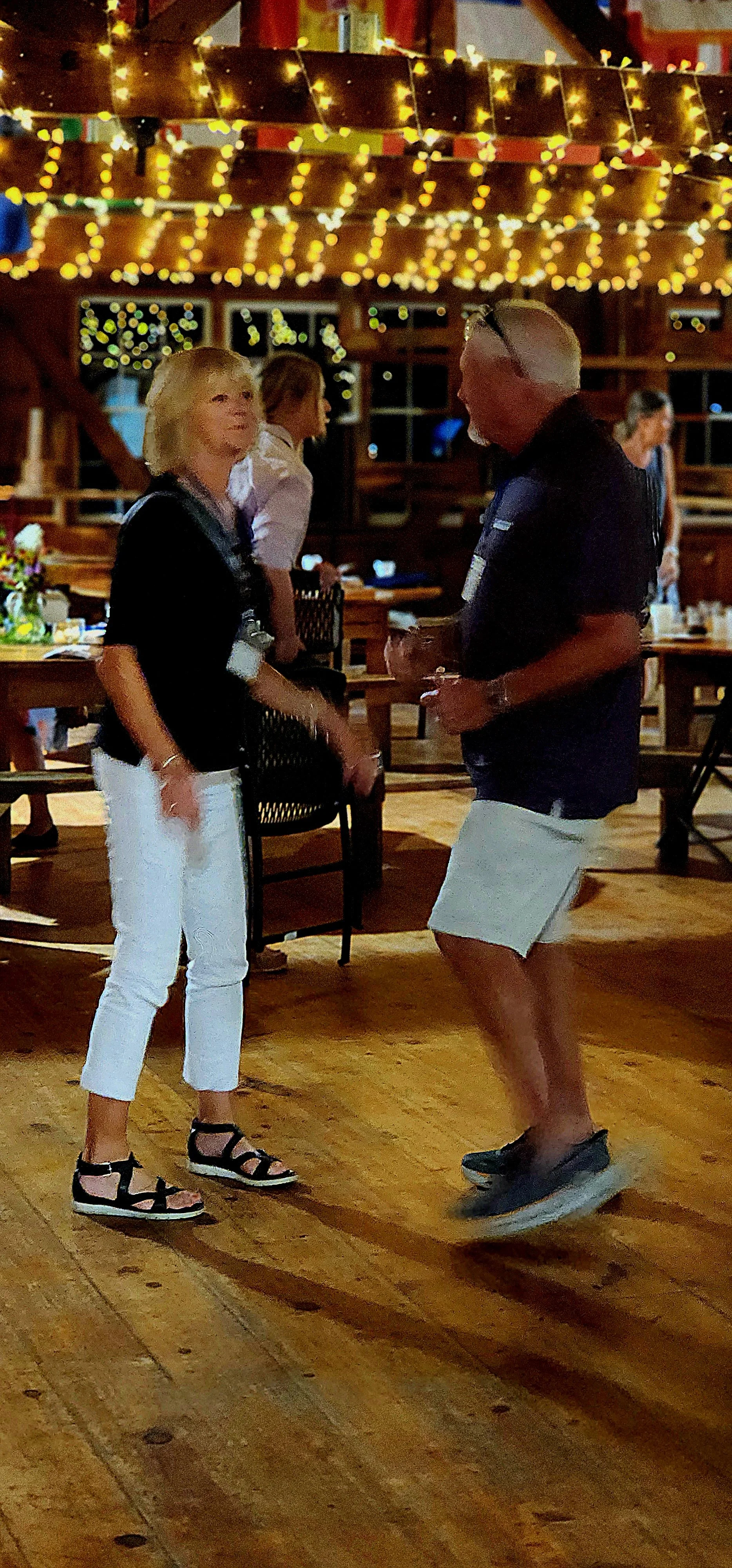 A woman, wearing a black shirt and white pants, and a man, wearing a black polo and white shorts, dancing