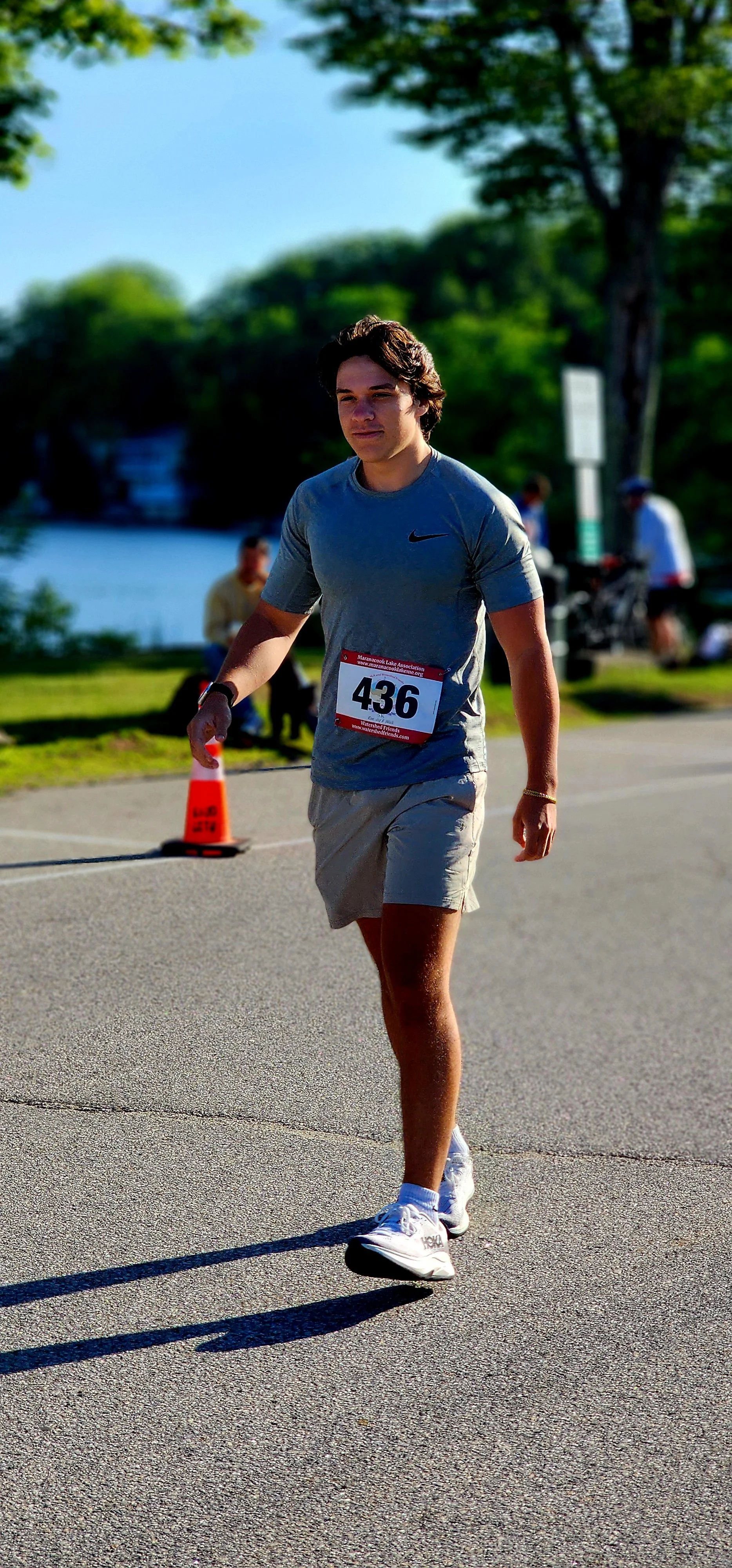 A man wearing a grey shirt and grey shorts, walking with a lake in the background