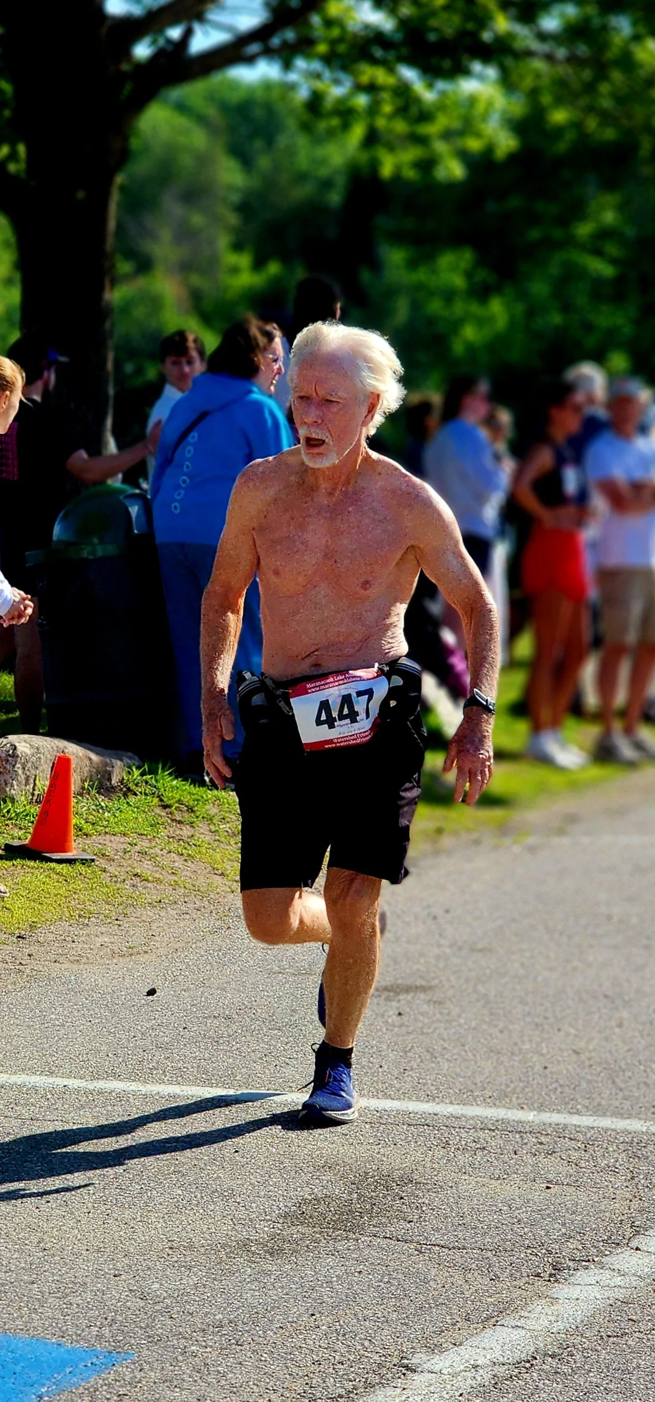 A shirtless man wearing black shorts running with a crowd standing in the background