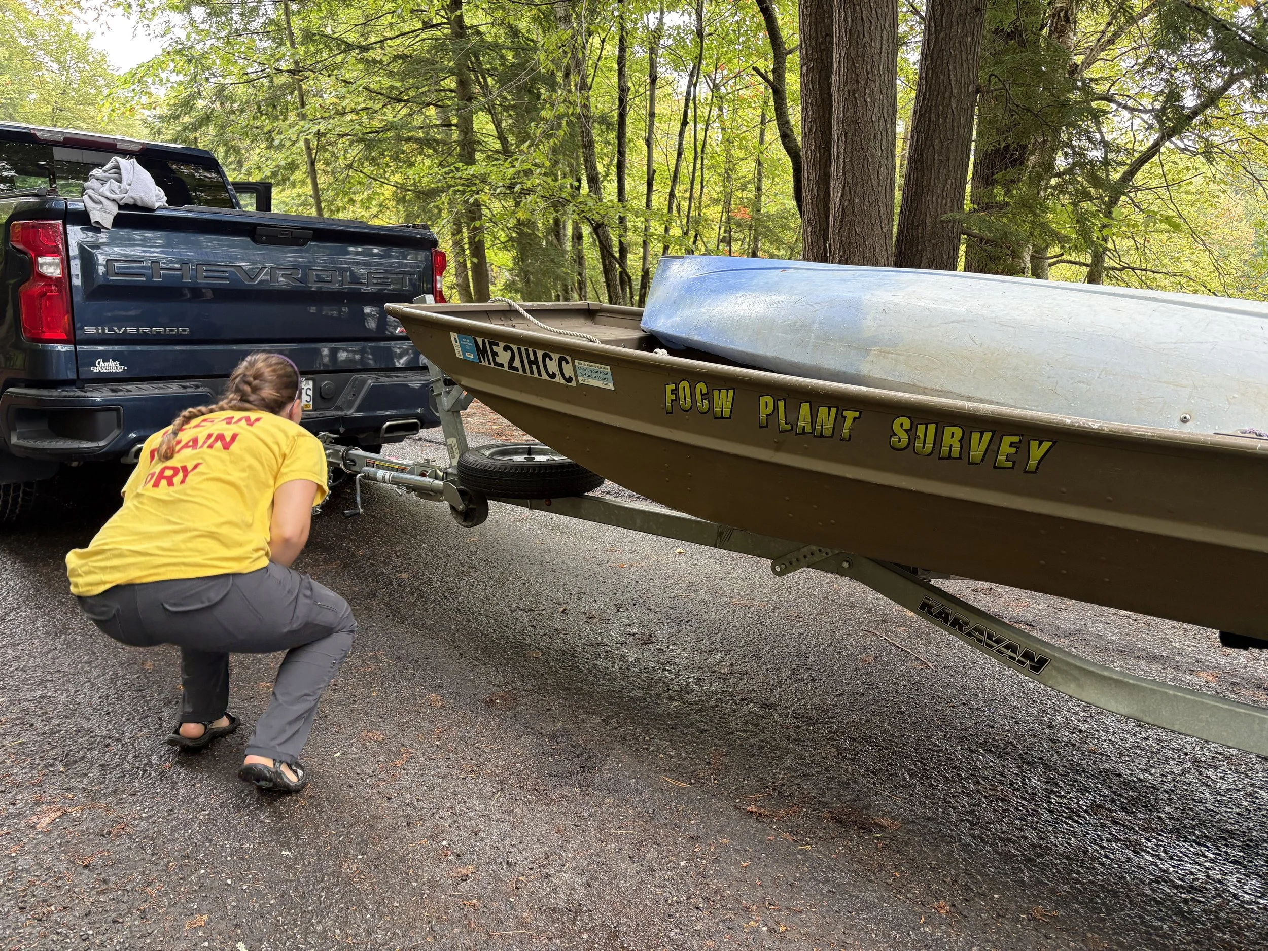 A woman wearing a yellow t-shirt, crouched next to a boat on a trailer