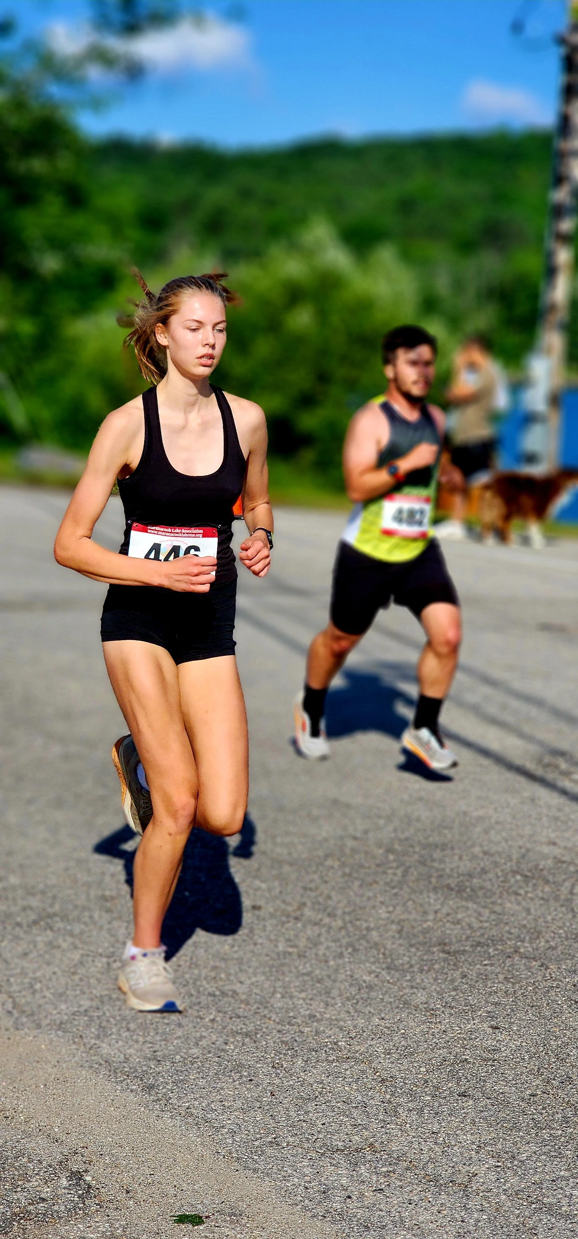 A woman wearing a black tank top and shorts running with a man wearing a black and yellow tank top and black shorts running behind her