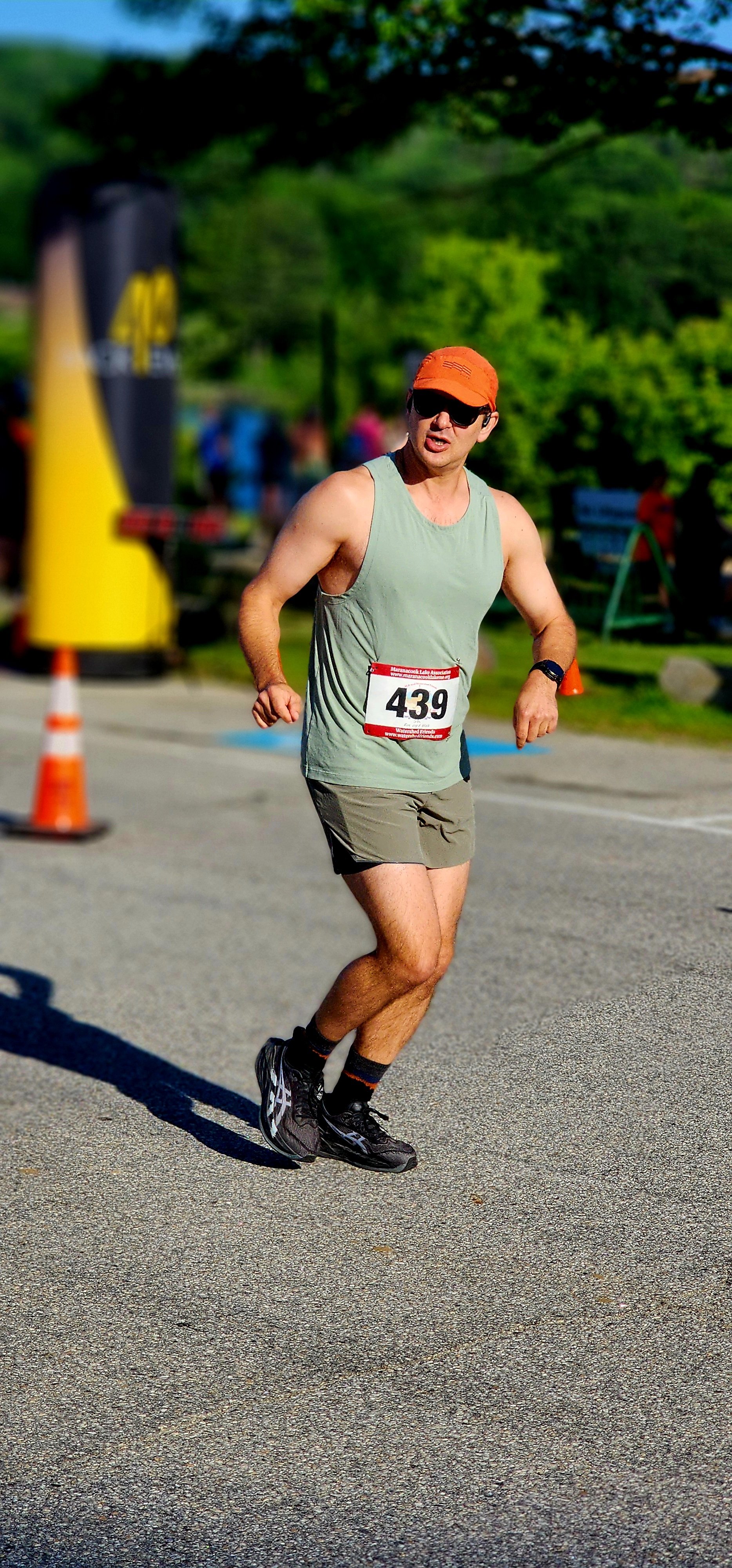 A man wearing a light grey tank top, grey shorts, and an orange ball cap, jogging
