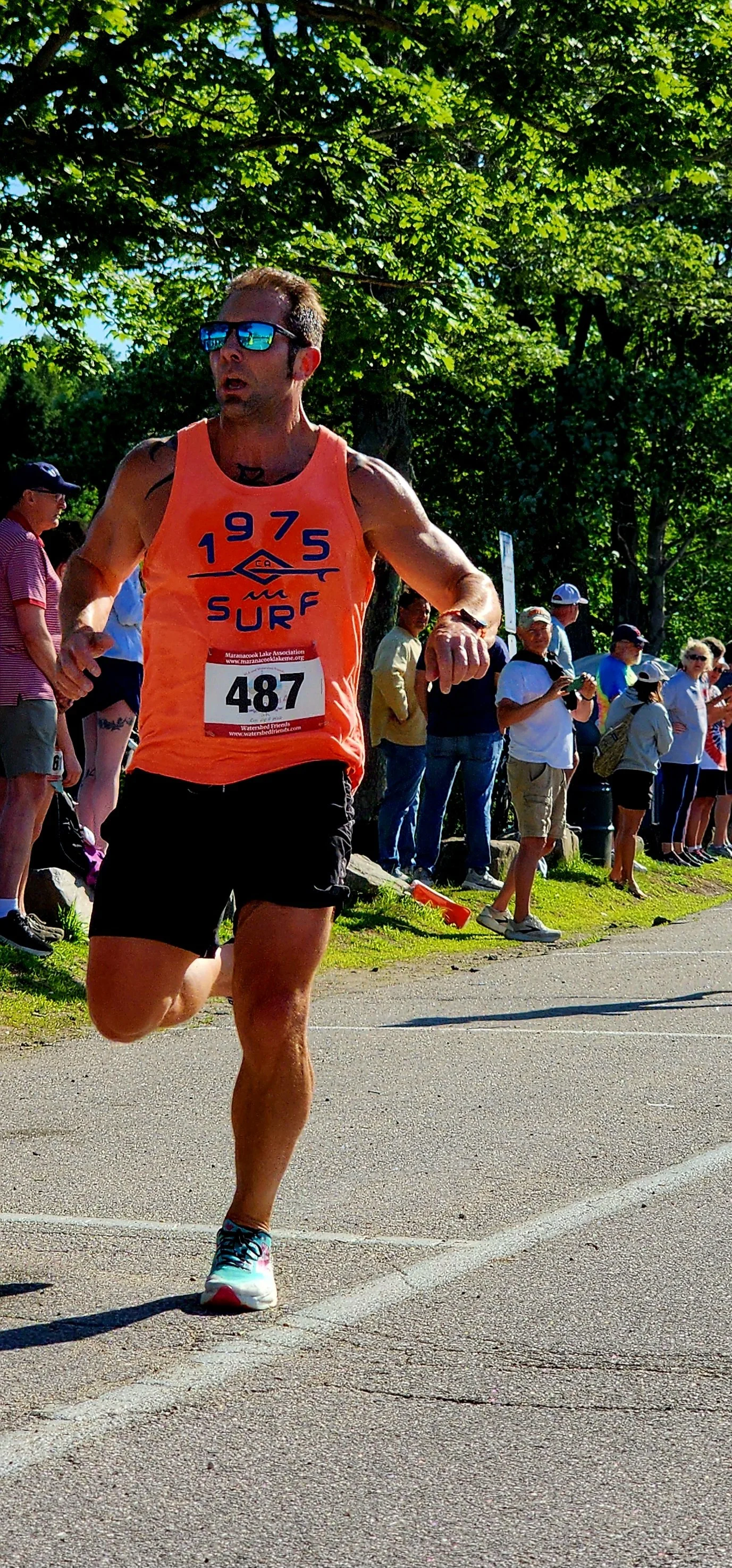 A man wearing an orange tank top and black shorts running with a crowd standing in the background