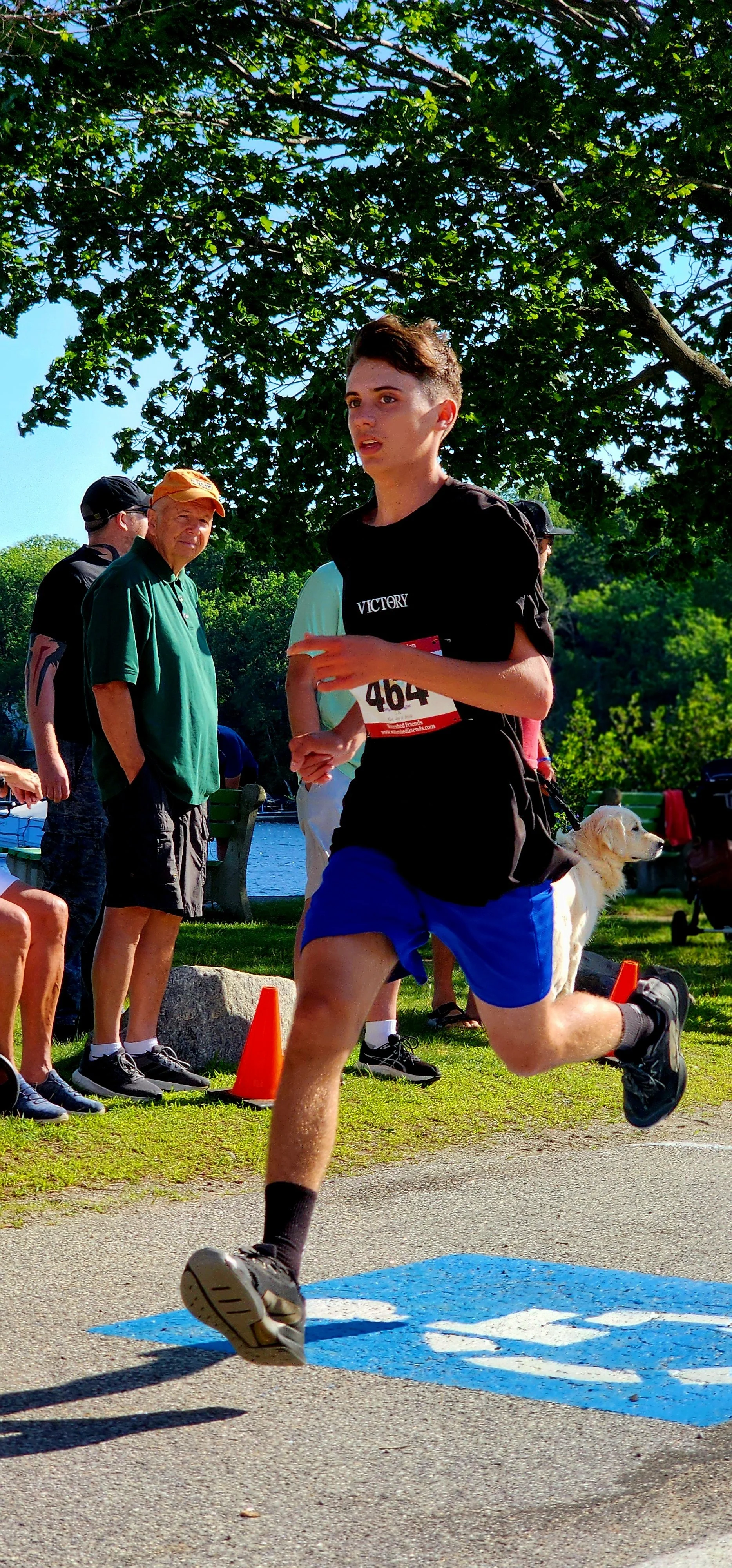A man wearing a black t-shirt and blue shorts running with a crowd standing the background