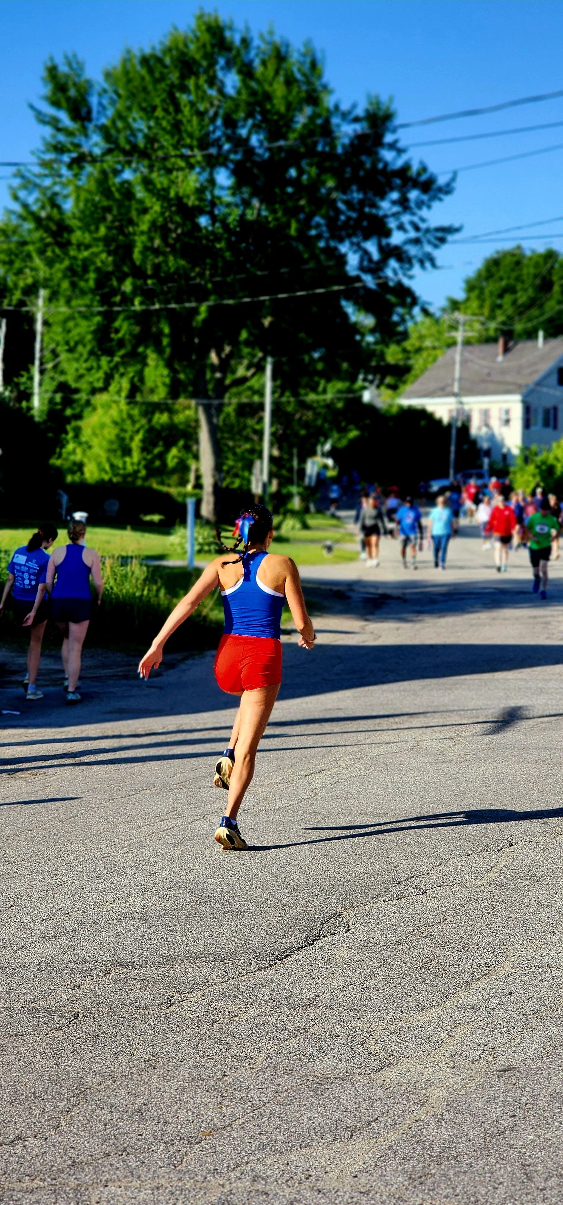 A woman, wearing a blue tank top and red shorts, facing away from the camera and skipping