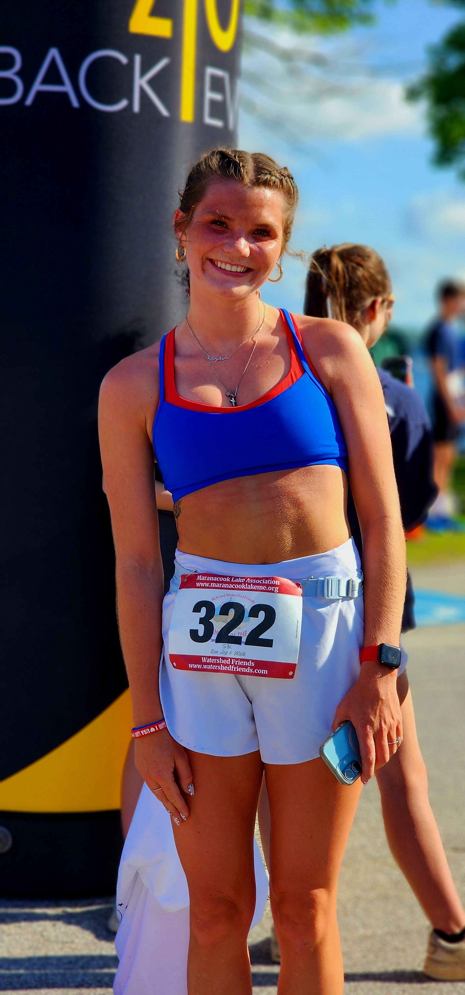 A woman wearing a blue cropped tank top and white shorts smiling at the camera in the finish area