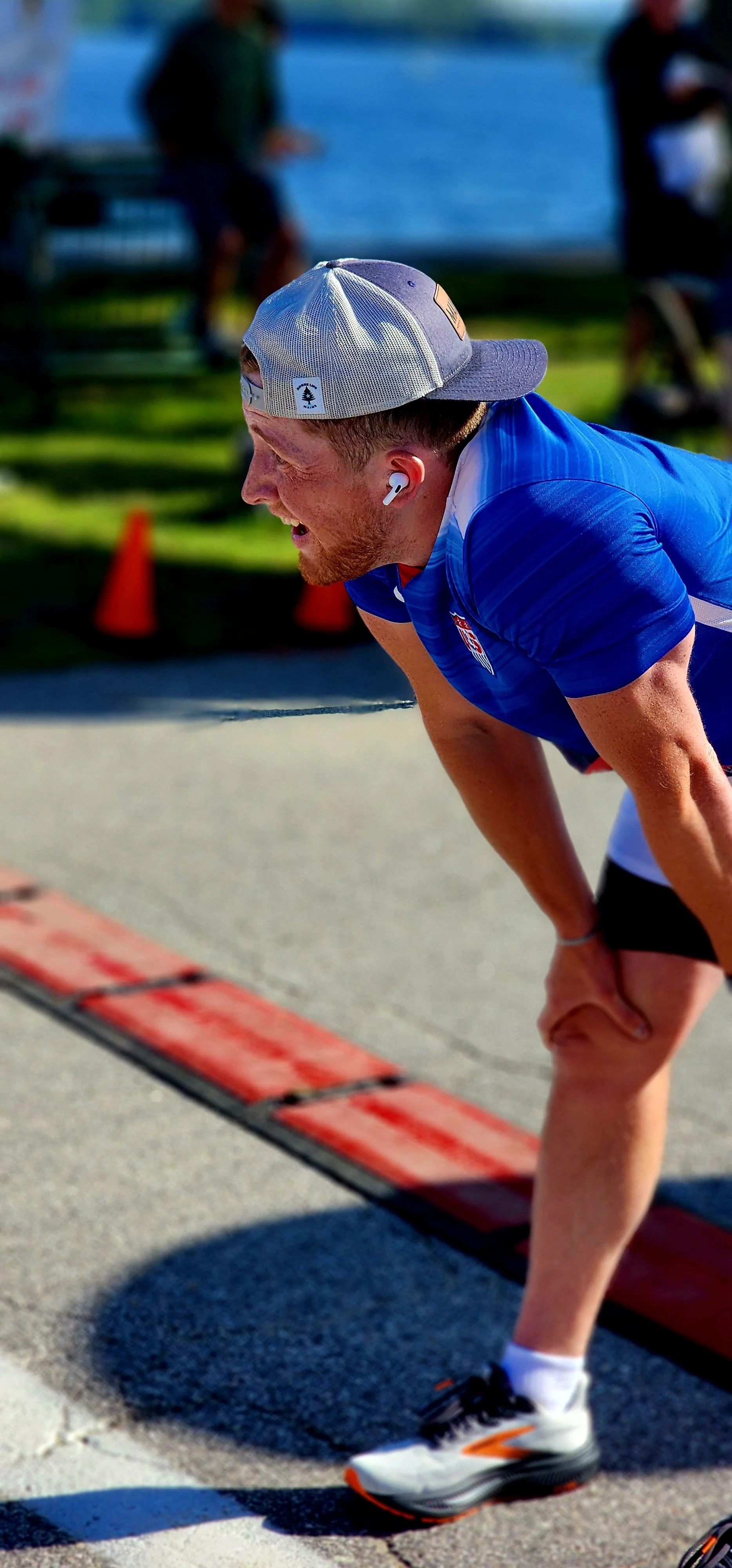 A man, wearing a blue t-shirt, taking a deep breath with his hands on his knees just past the finish line