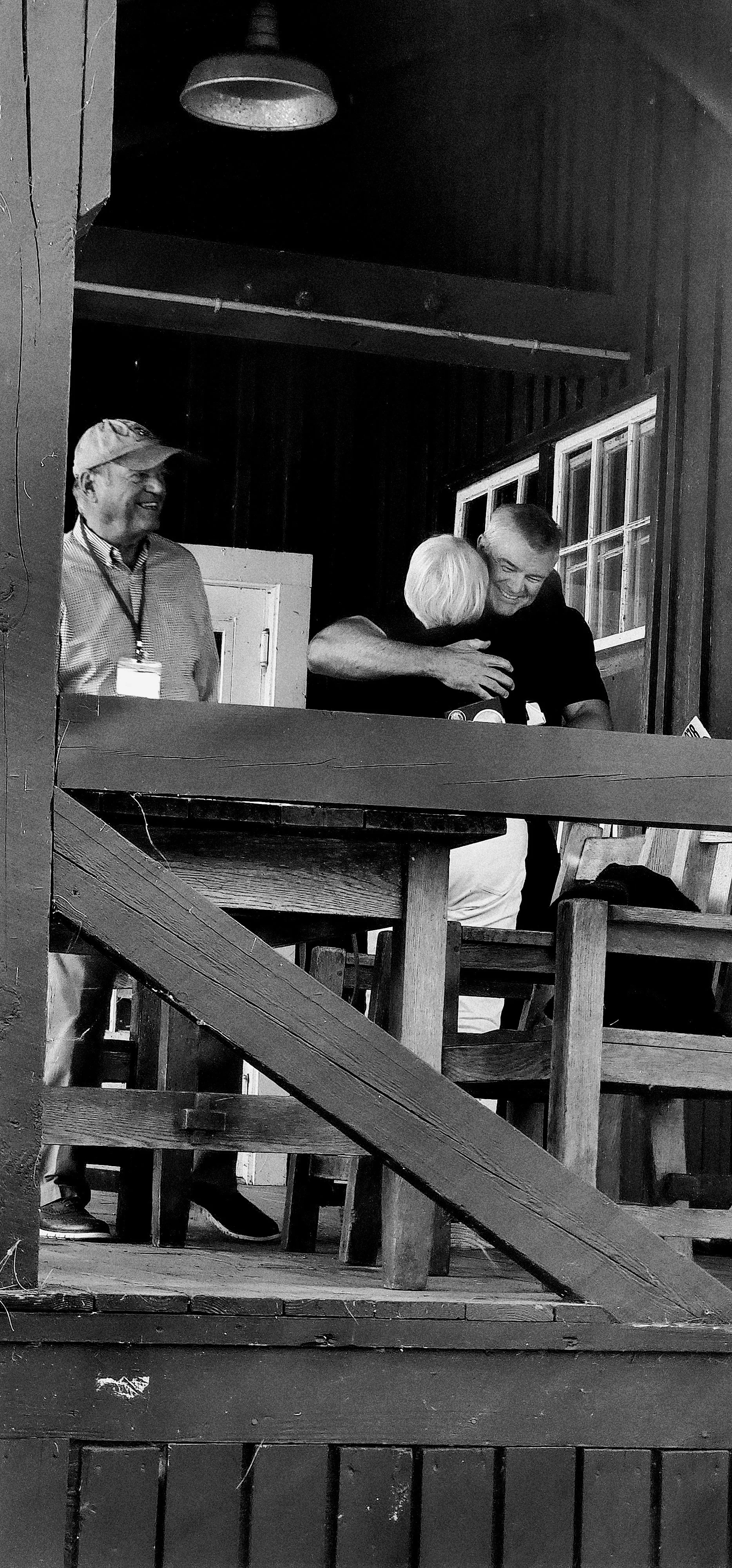 Two people hugging on a porch with a third person smiling at them