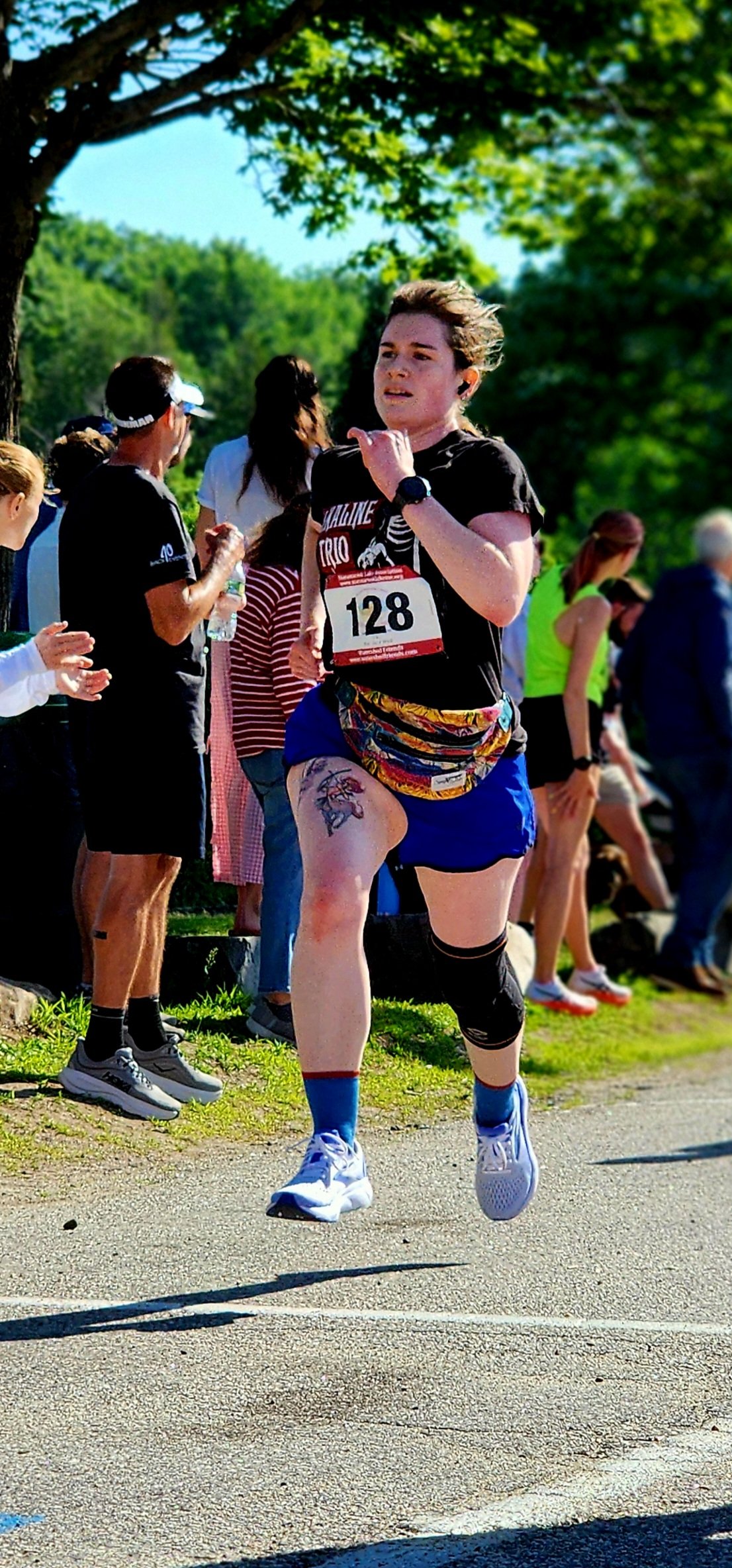 A person wearing a black t-shirt and black shorts running with a crowd standing in the background