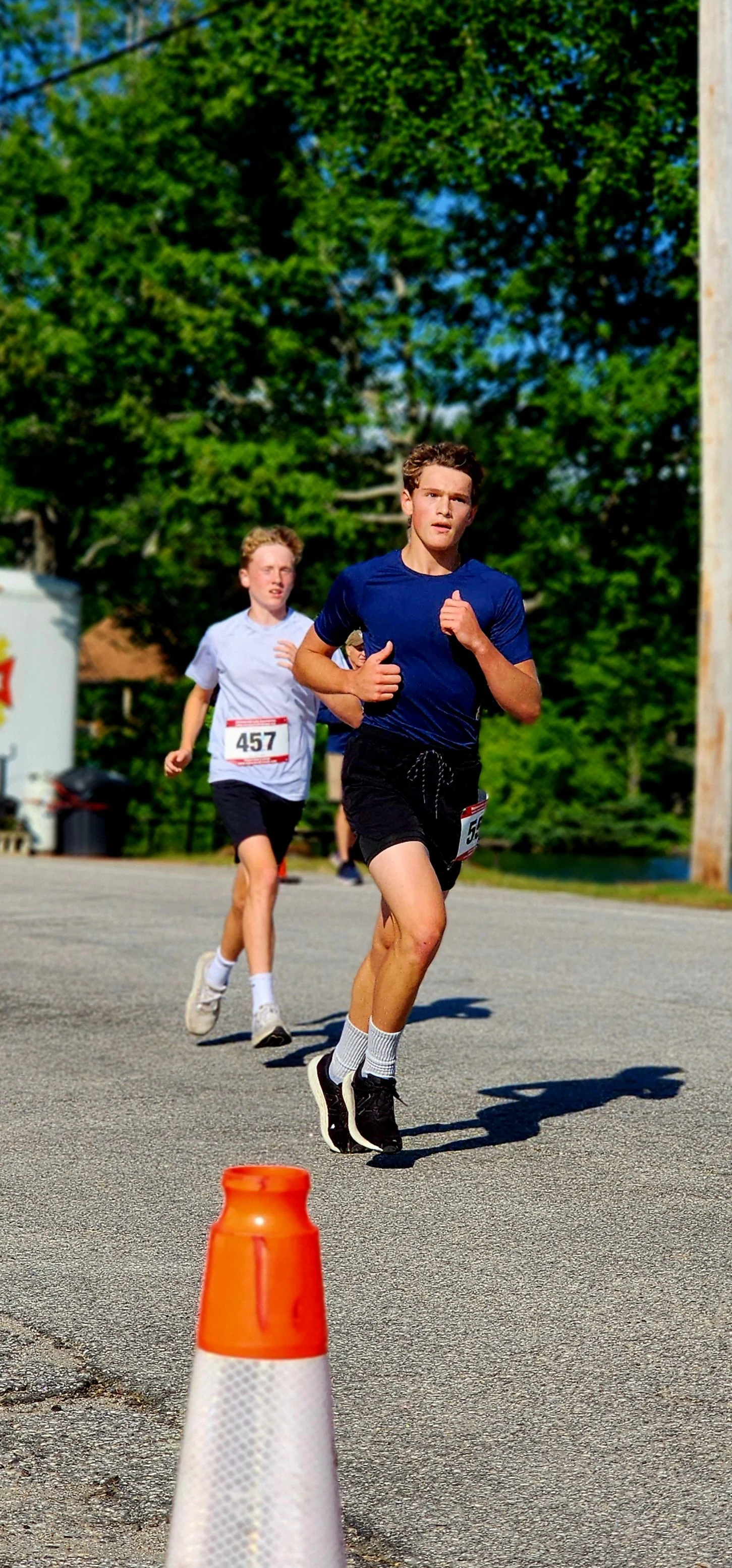 A man in a blue t-shirt and black shorts running with a person in a white t-shirt behind