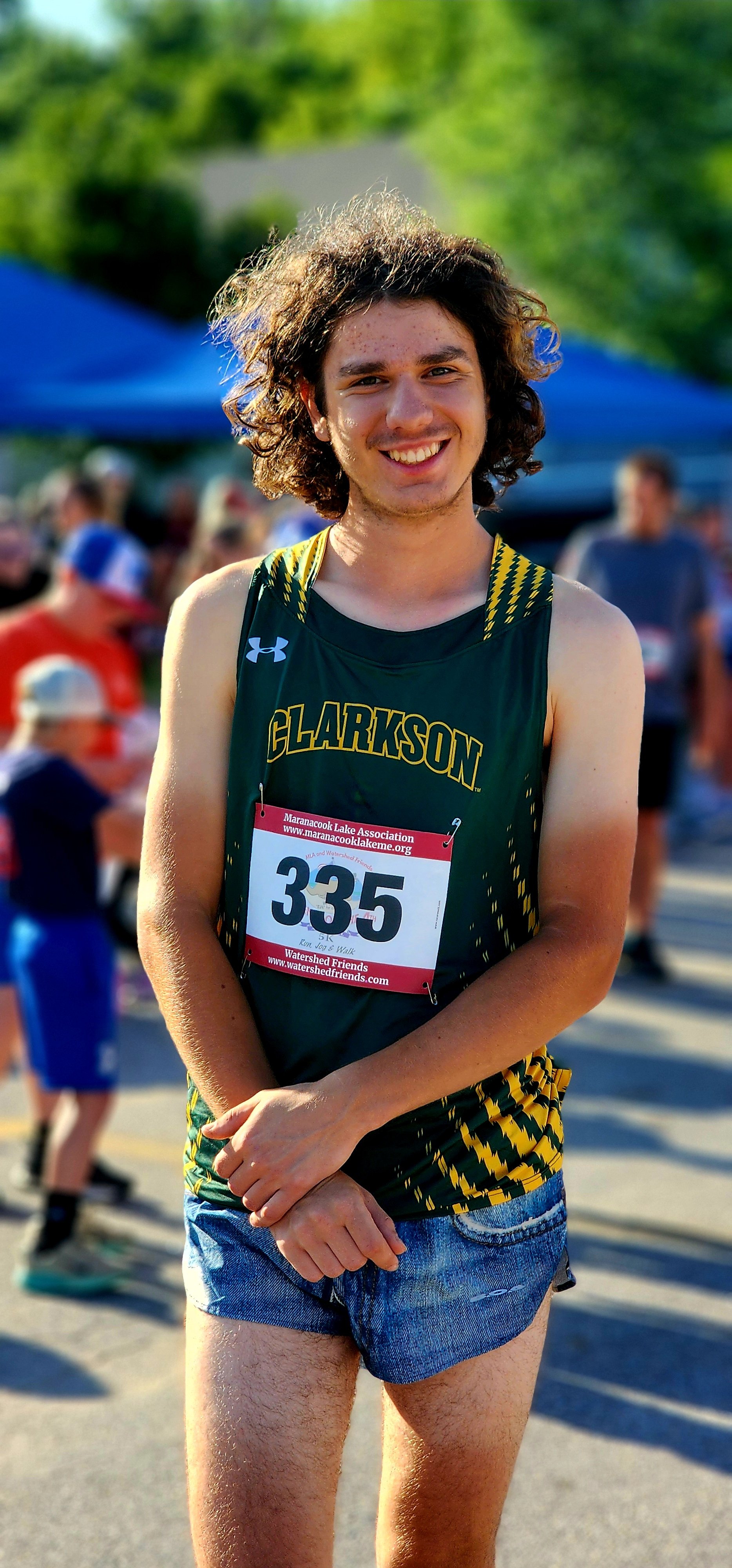 A man, wearing a green and yellow tank top and blue shorts, smiling at the camera