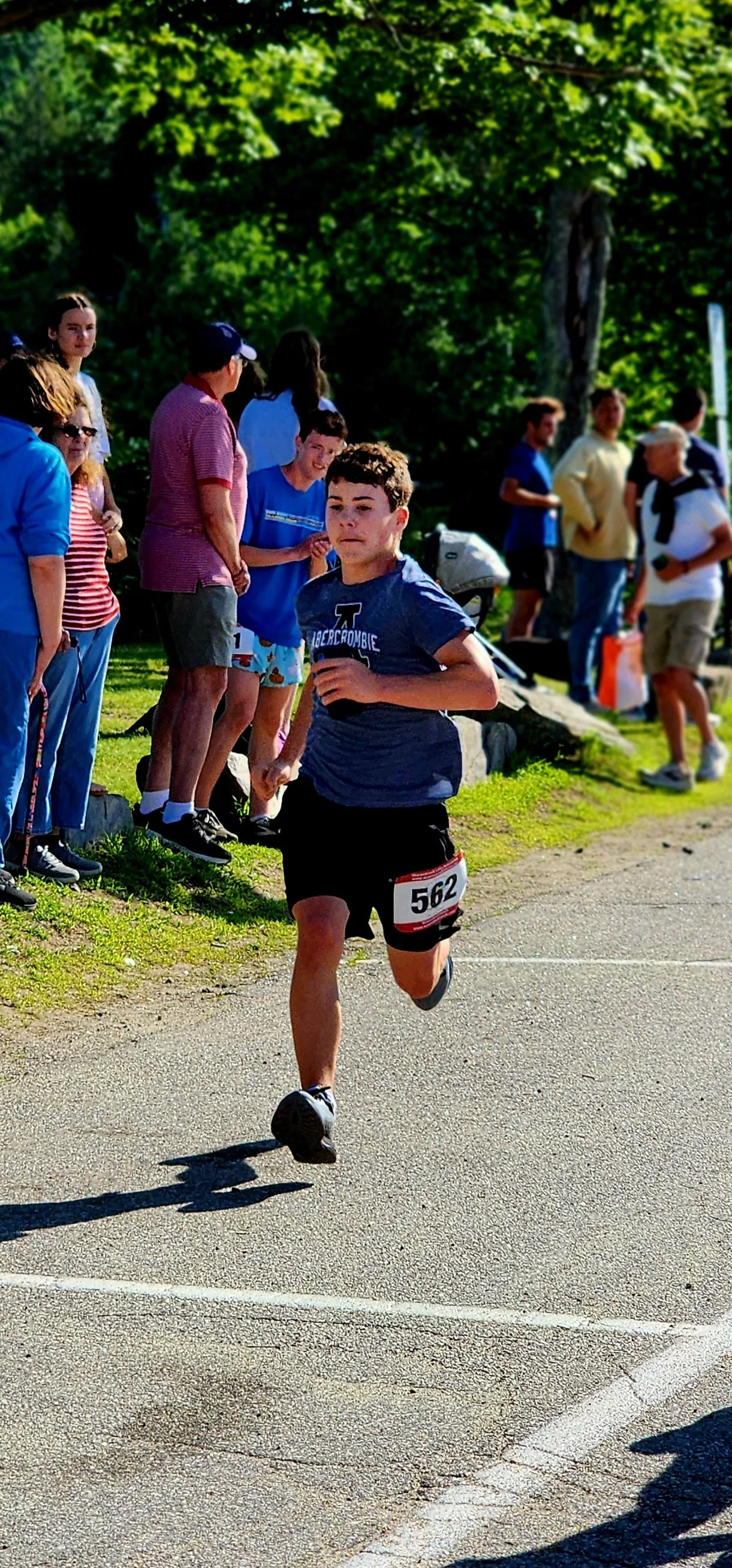 A man wearing a blue t-shirts and black shorts running with a crowd standing in the background