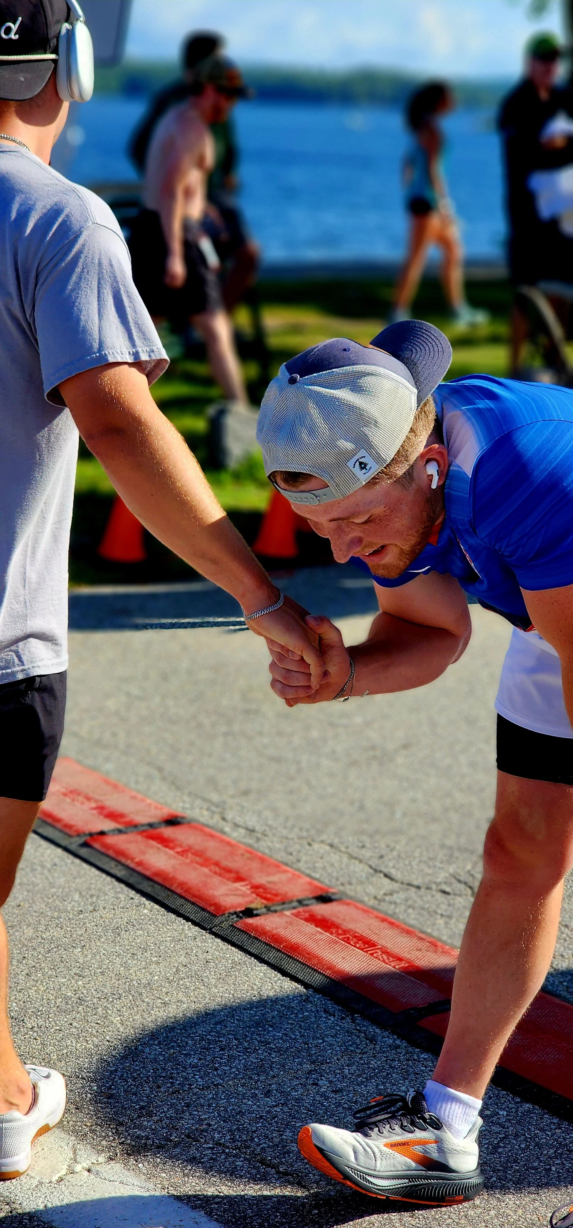 Two men clasping hands just past the finish line, one bend over the other facing away from the camera
