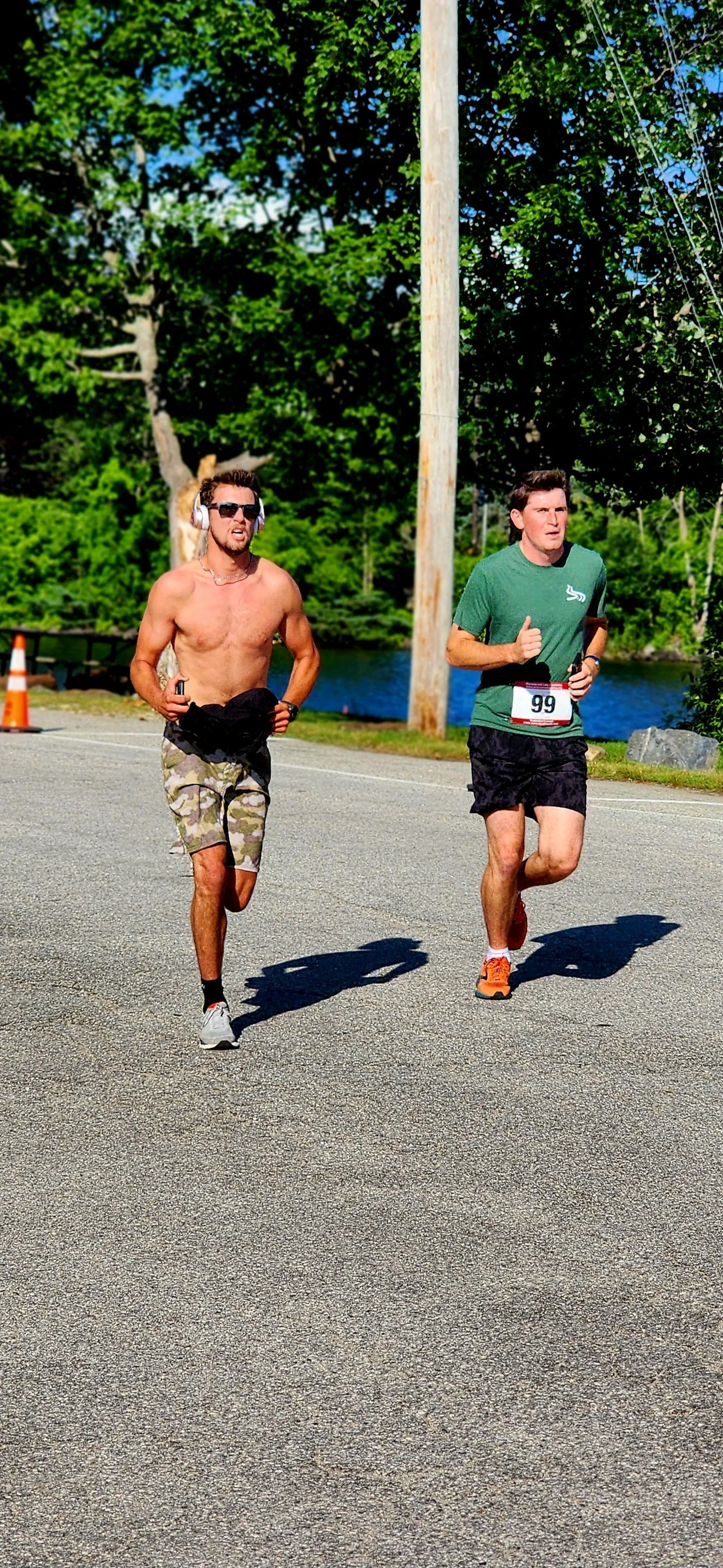 A shirtless man wearing khaki camo patterned shorts running beside a man wearing a green t-shirt and black shorts