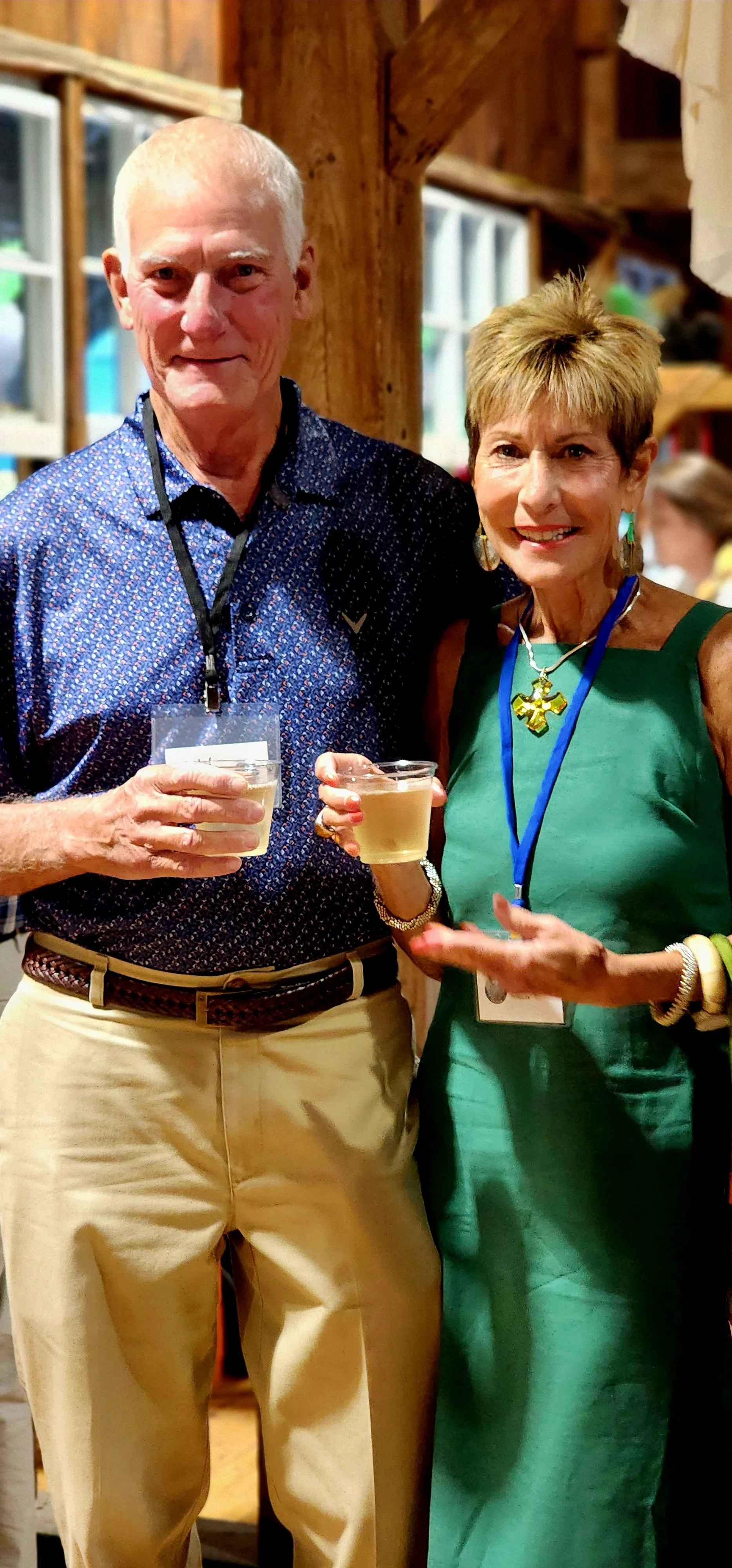 A man, wearing a navy polo and khakis, and a woman, wearing a green dress, smiling at the camera
