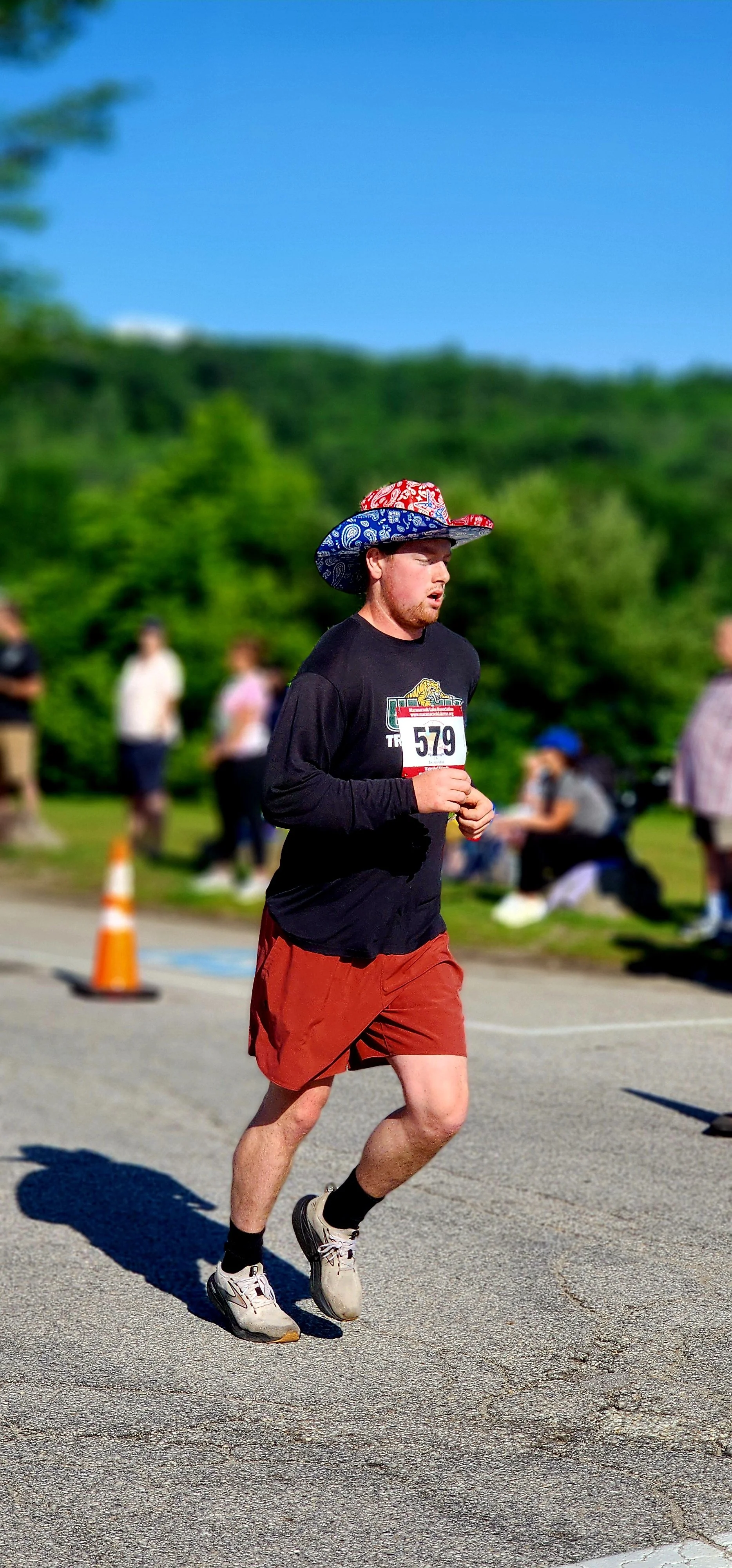 A man wearing a patriotic cowboy hat, black long sleeve shirt, and red shorts running