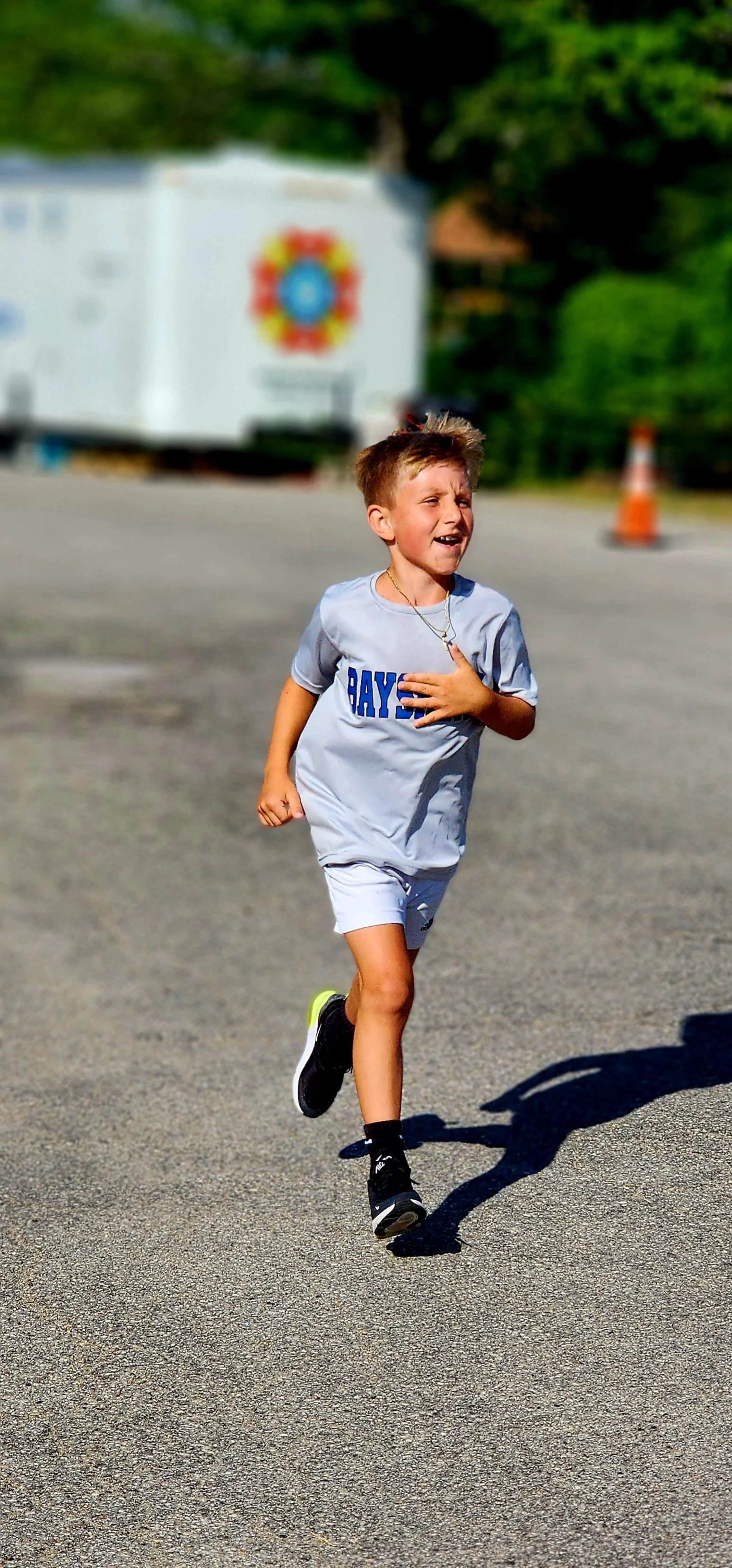 A young boy wearing a grey t-shirt and shorts running 