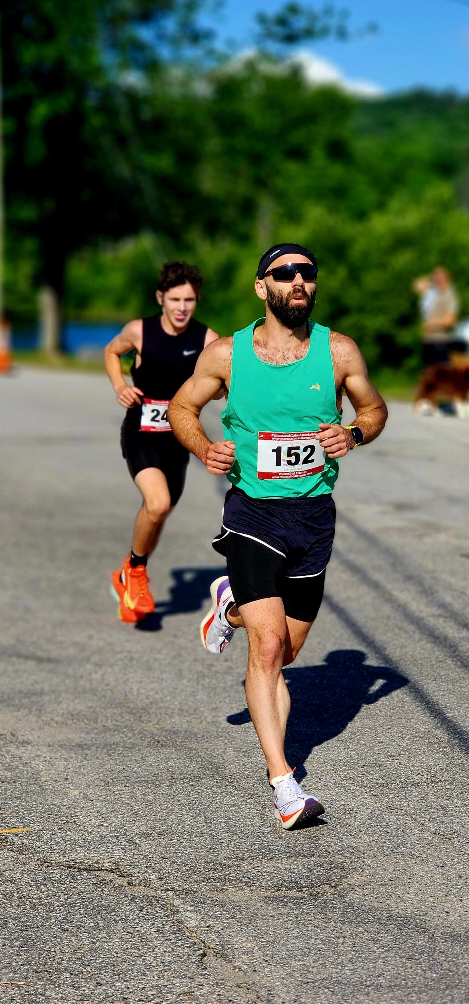 A man in a green tank top and black shorts running in front of a person wearing a black tank top and black shorts