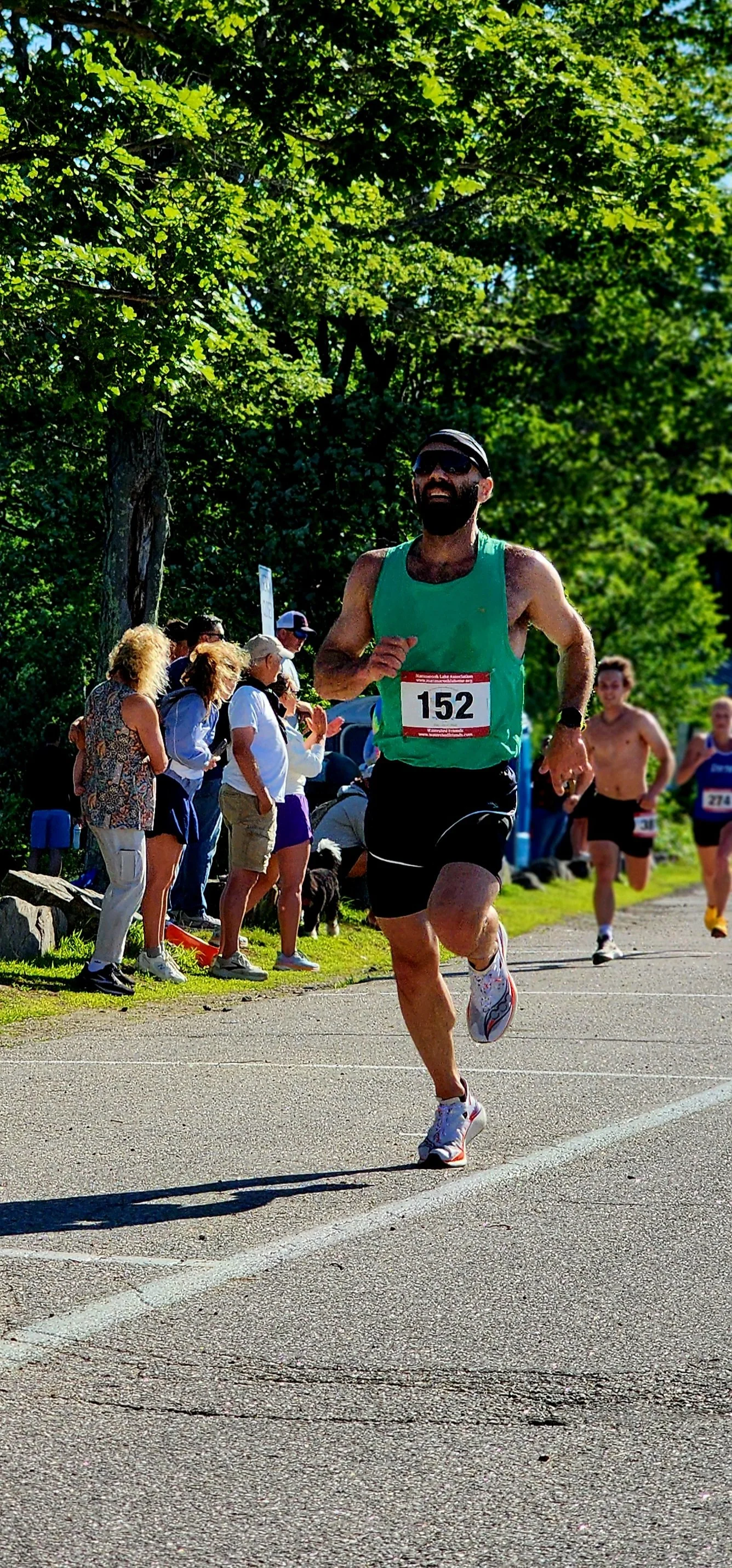 A man wearing a green tank top and black shorts running with a crowd standing behind him